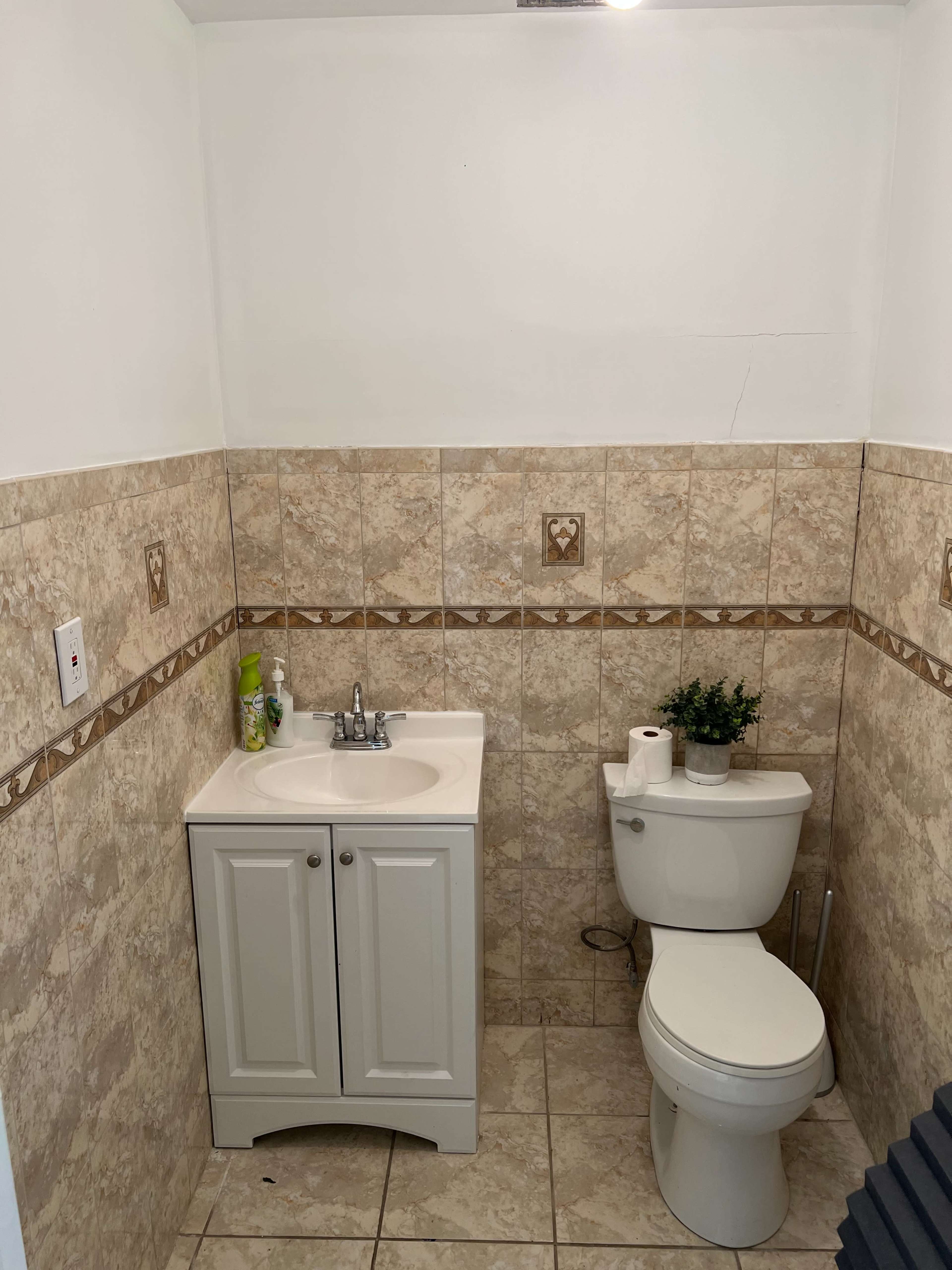 A small bathroom featuring a white vanity with a sink and a toilet, with tiled walls and floor.