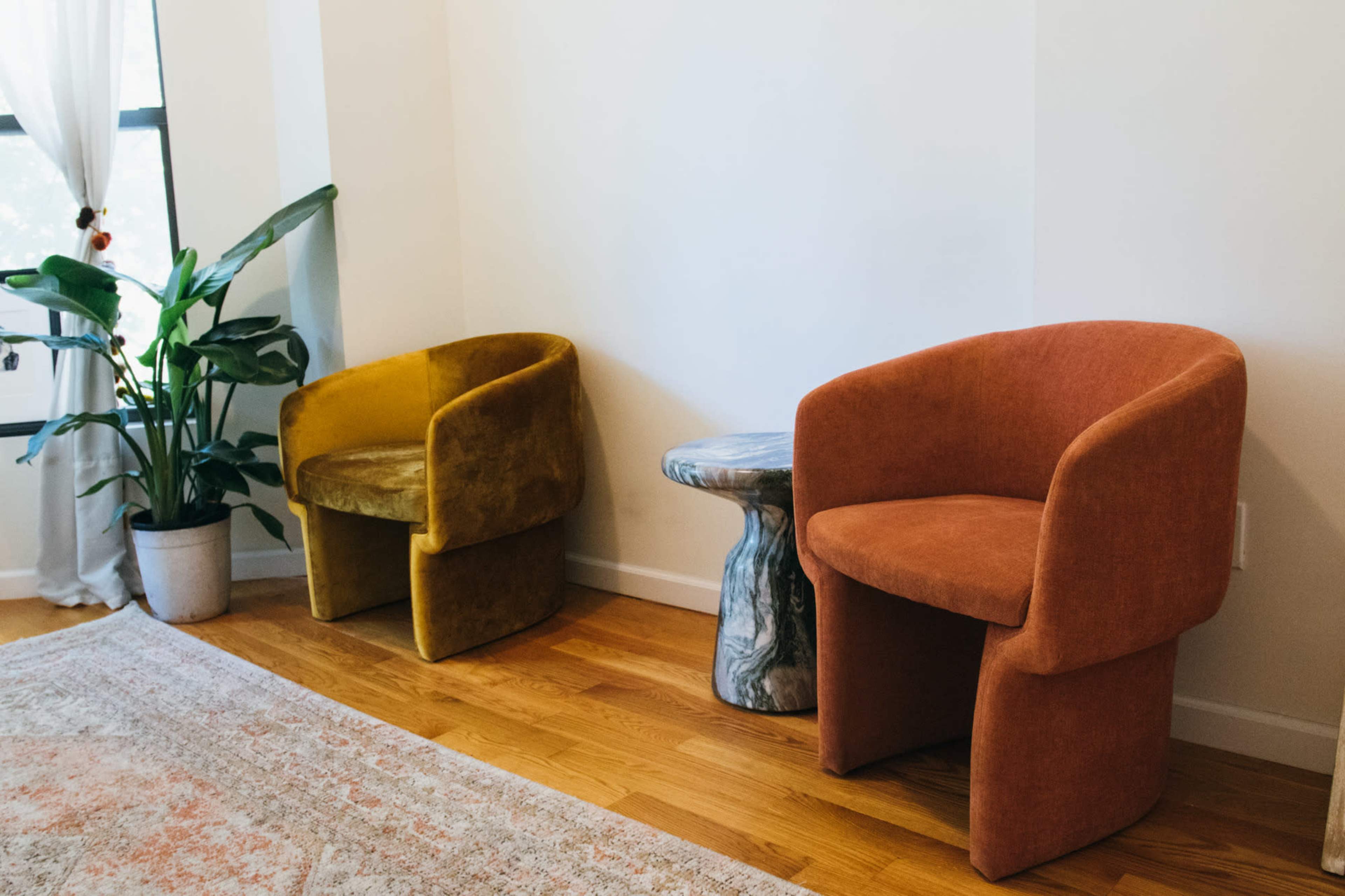 Two upholstered chairs in yellow and orange are positioned beside a textured stone side table in a brightly lit room with a potted plant.