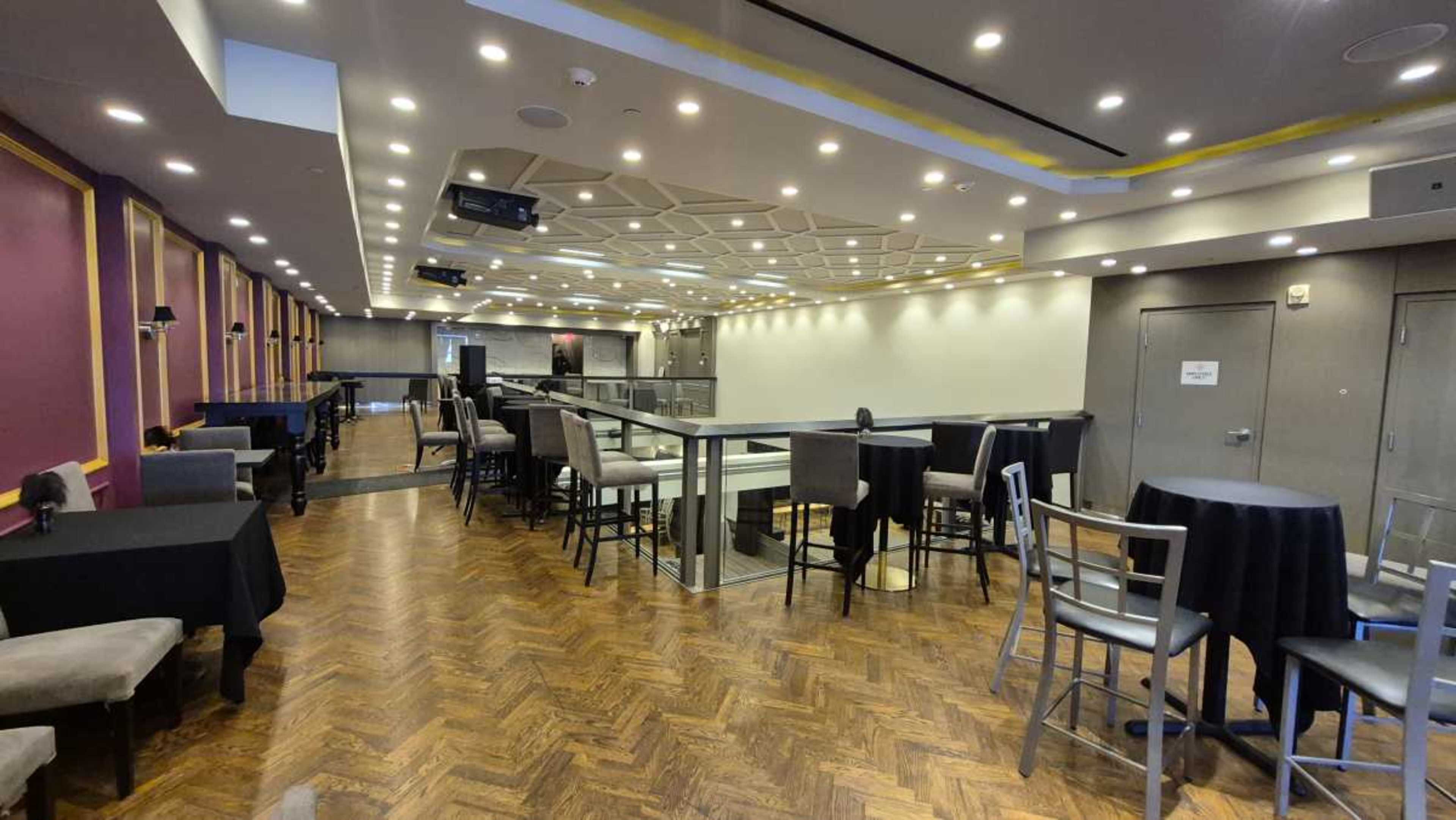 The image shows an interior space of a well-lit event venue featuring a mix of tables and chairs arranged around a central area.