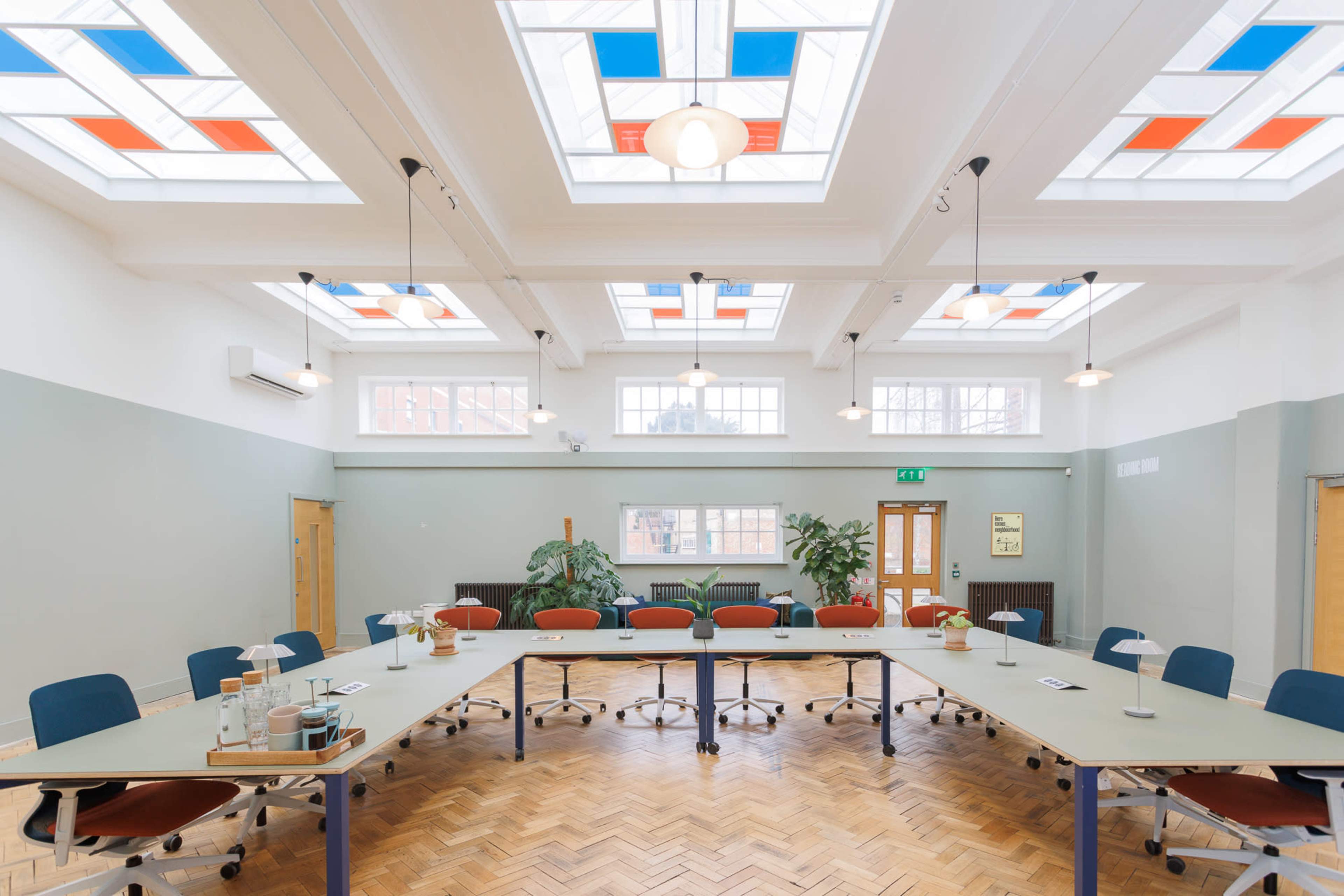 A spacious conference room features a large rectangular table surrounded by blue and orange chairs, with natural light filtering through decorative skylights.