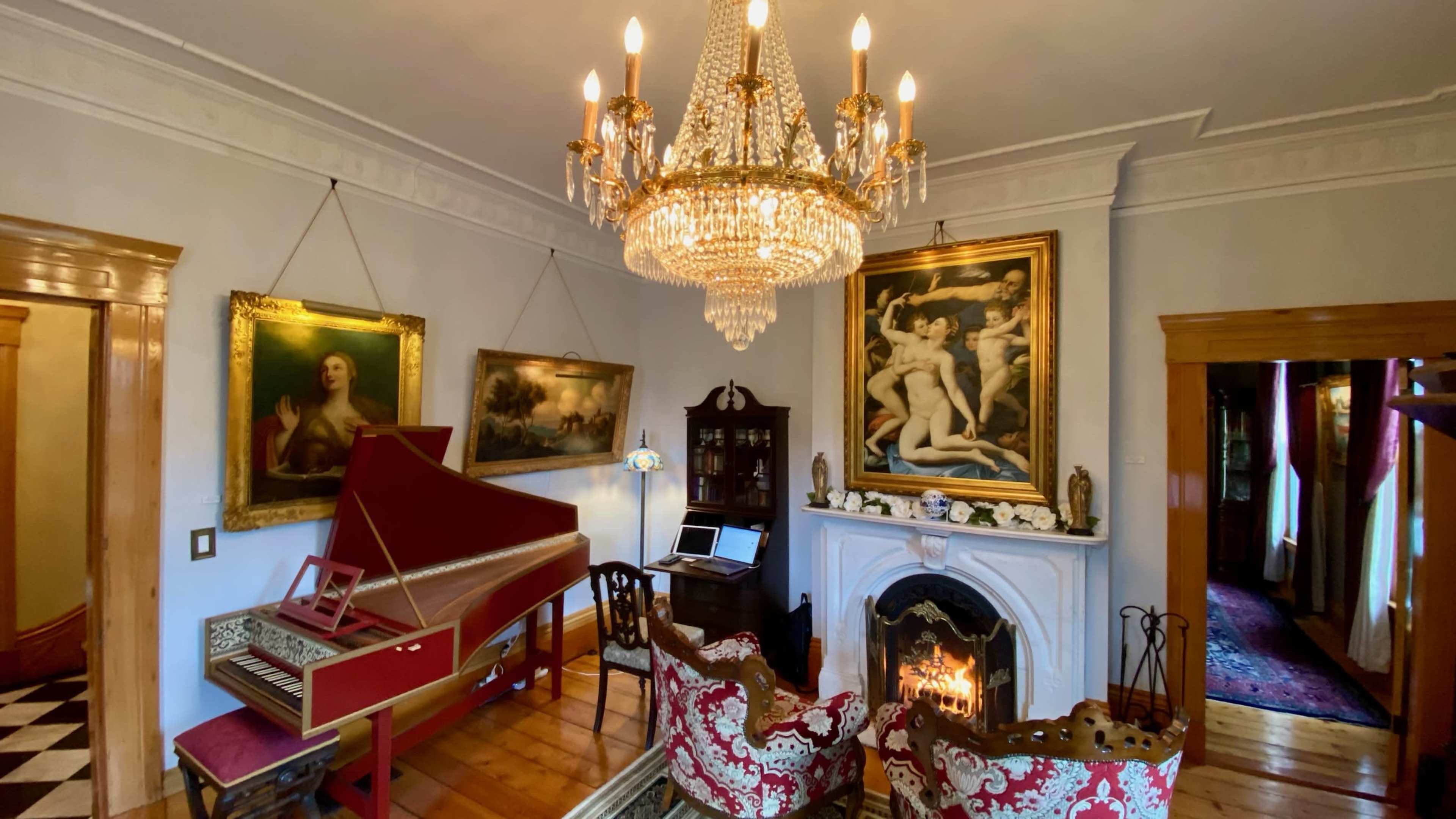 The image shows a room with a chandelier, a harpsichord, two ornate chairs, paintings on the walls, and a fireplace with a fire burning.