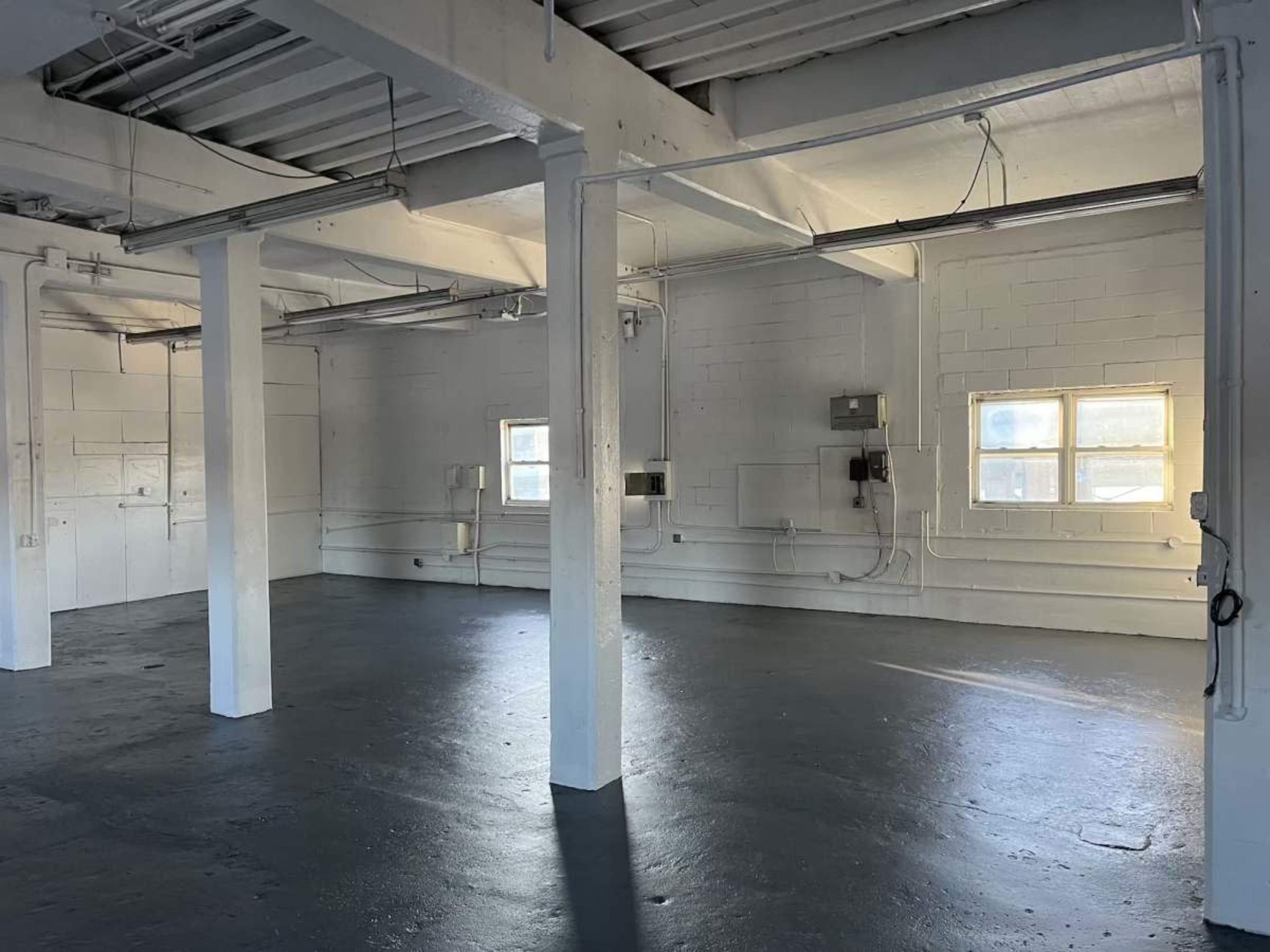 The image shows an empty, white-walled industrial space with concrete floors and several support columns.