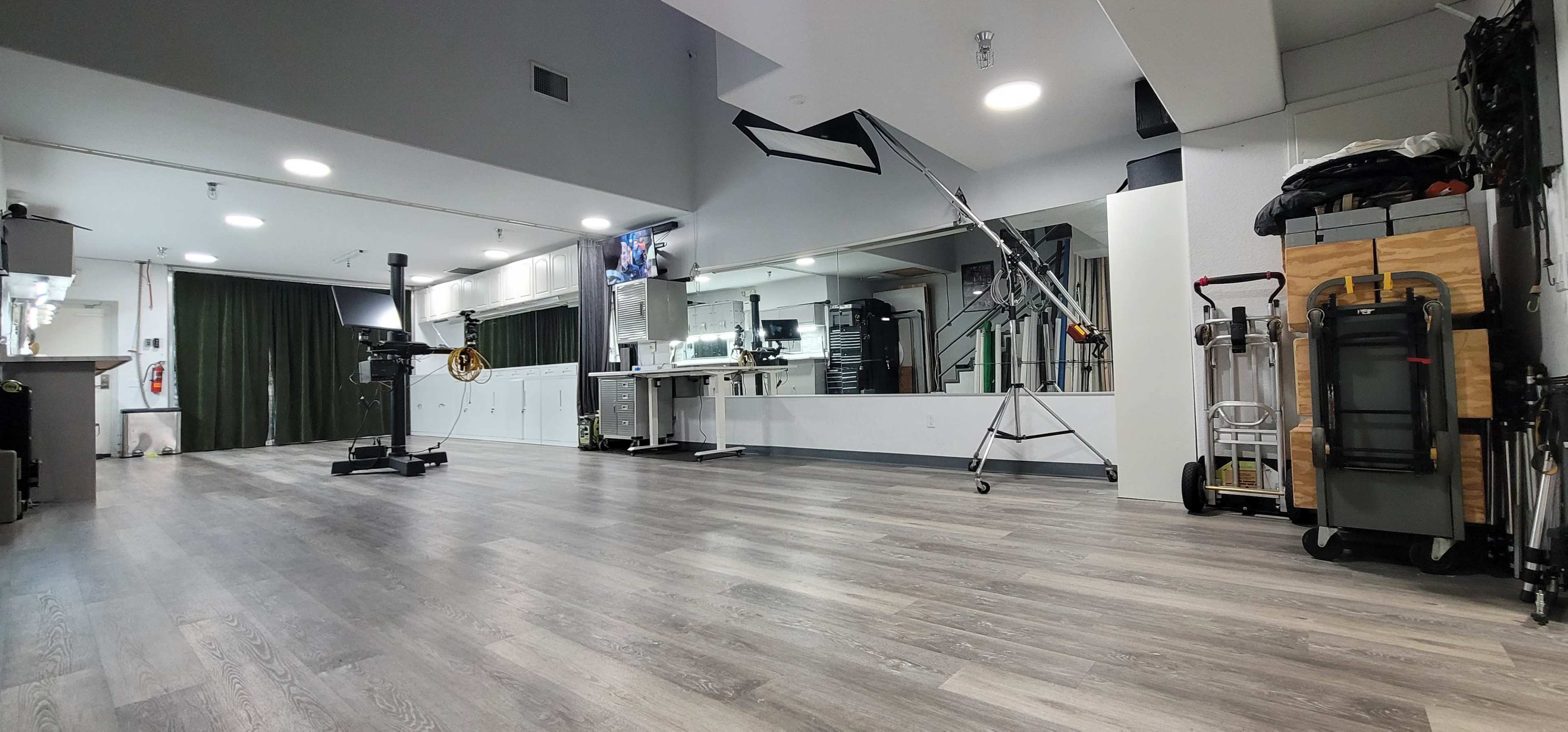 The image shows a spacious, modern studio with a polished wooden floor, featuring various equipment and a mirror across one wall.