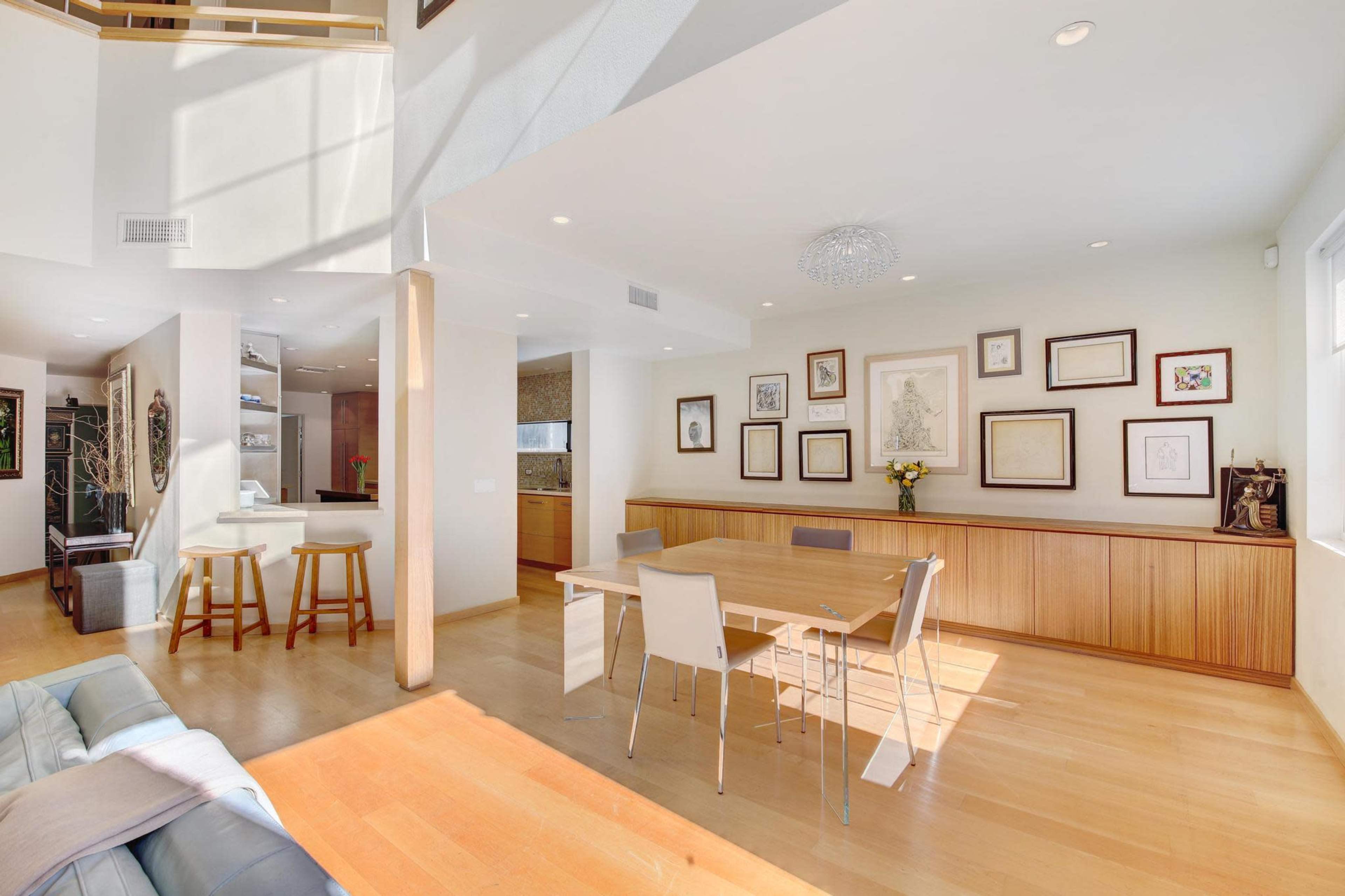 A modern, well-lit dining area featuring a wooden table surrounded by white chairs, with framed artwork displayed on the walls.