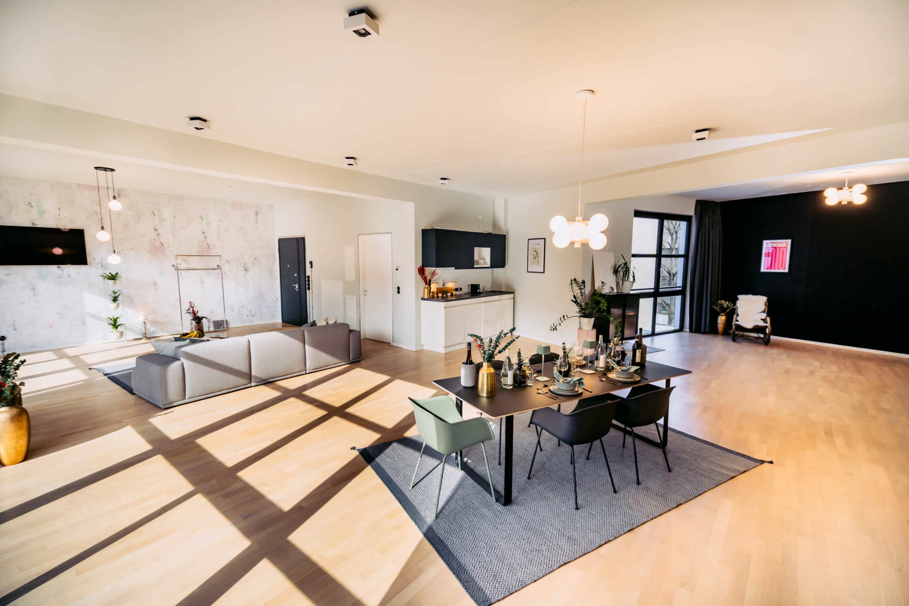 A contemporary open-plan living and dining area with a modern kitchen, featuring a dining table set for a meal and a large sofa in the seating area.