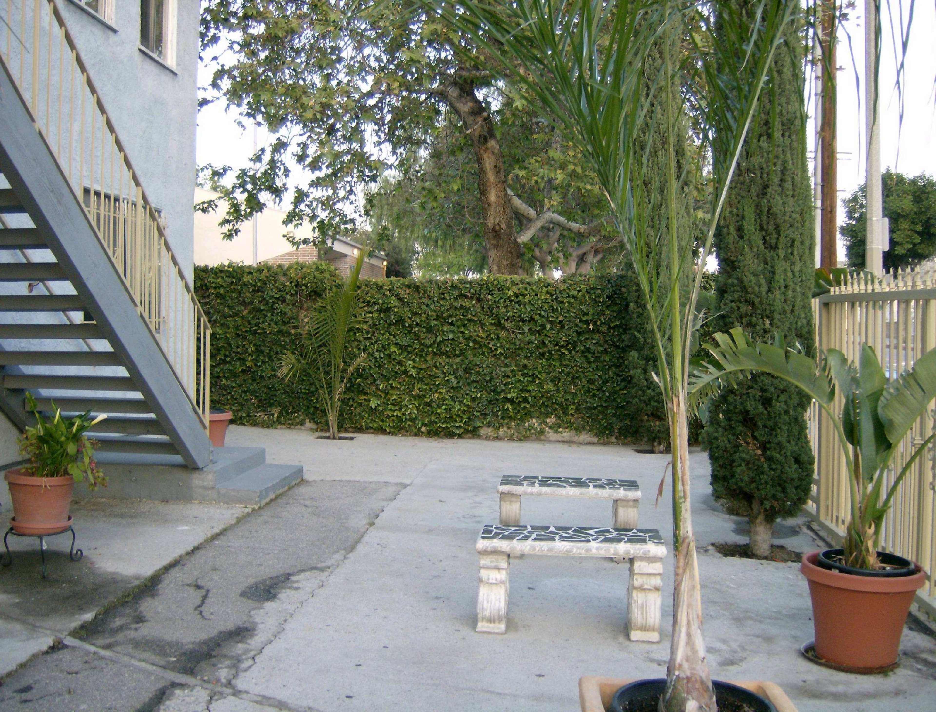 The image shows a concrete outdoor space with a bench, potted plants, and a staircase leading up to a building.