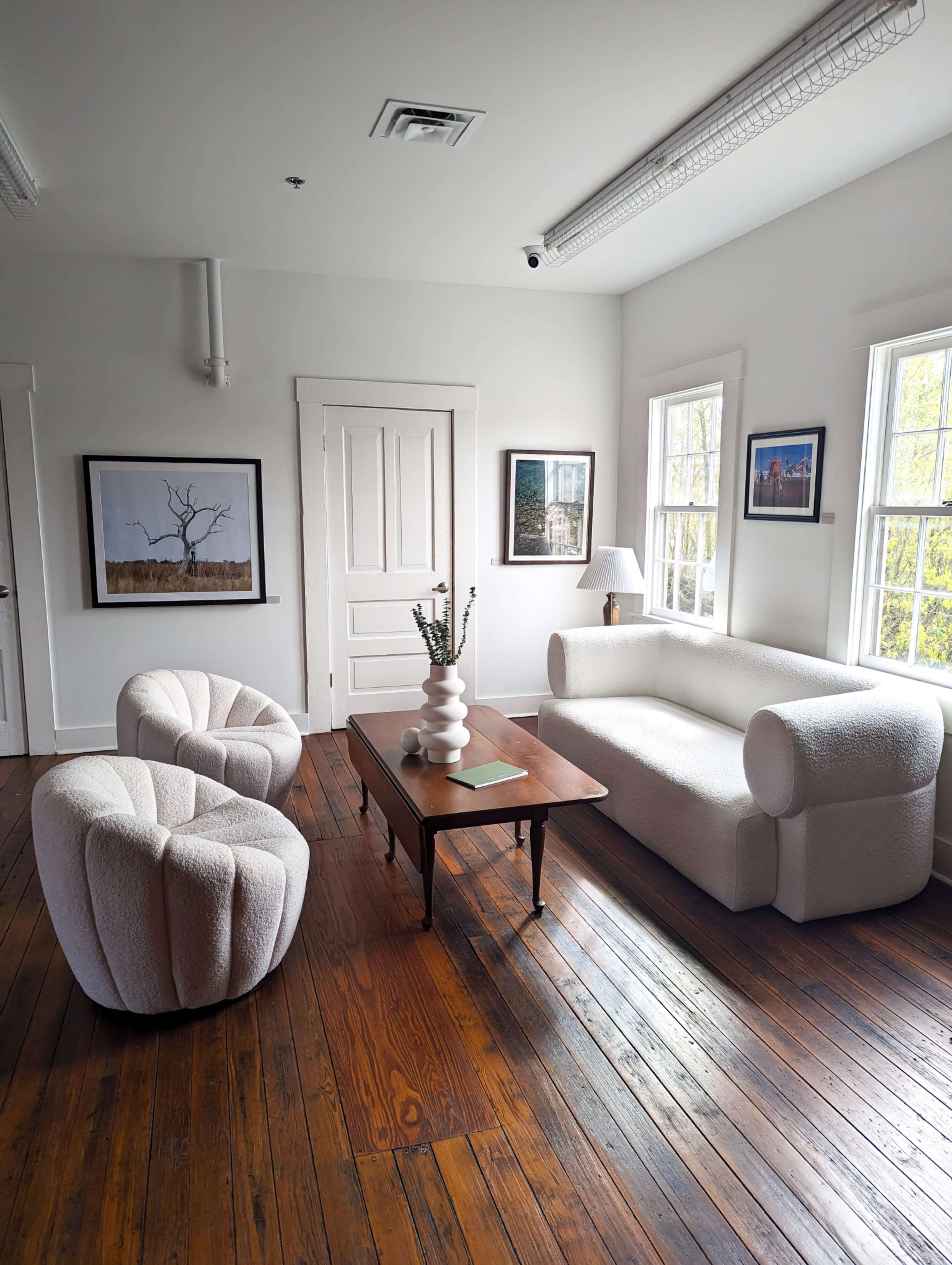 A modern living room with a white sofa, two textured armchairs, a wooden coffee table, and framed artwork on the walls.