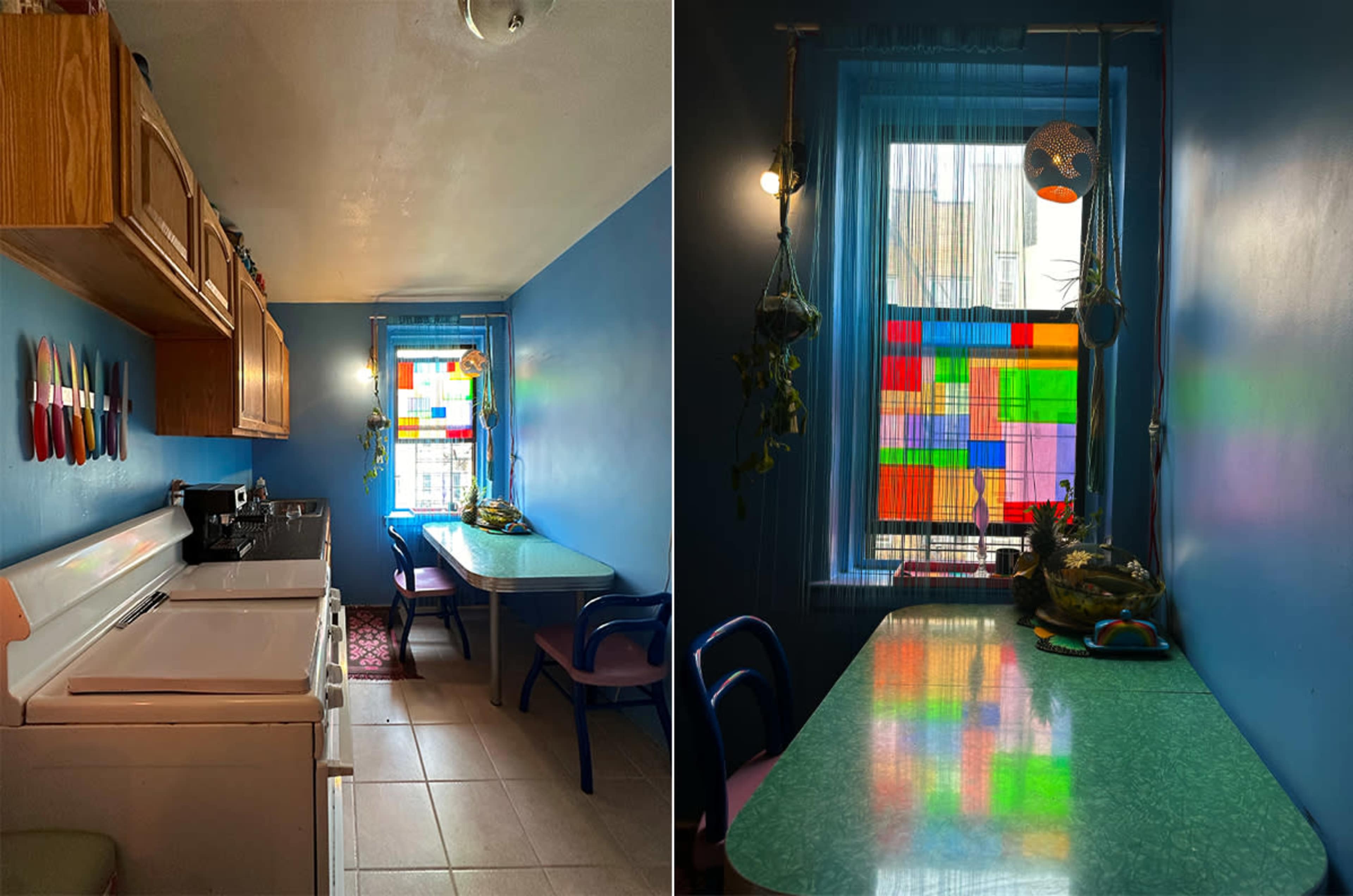 The image shows a kitchen with blue walls, wooden cabinets, a white stove, and a table near a window displaying colorful stained glass.