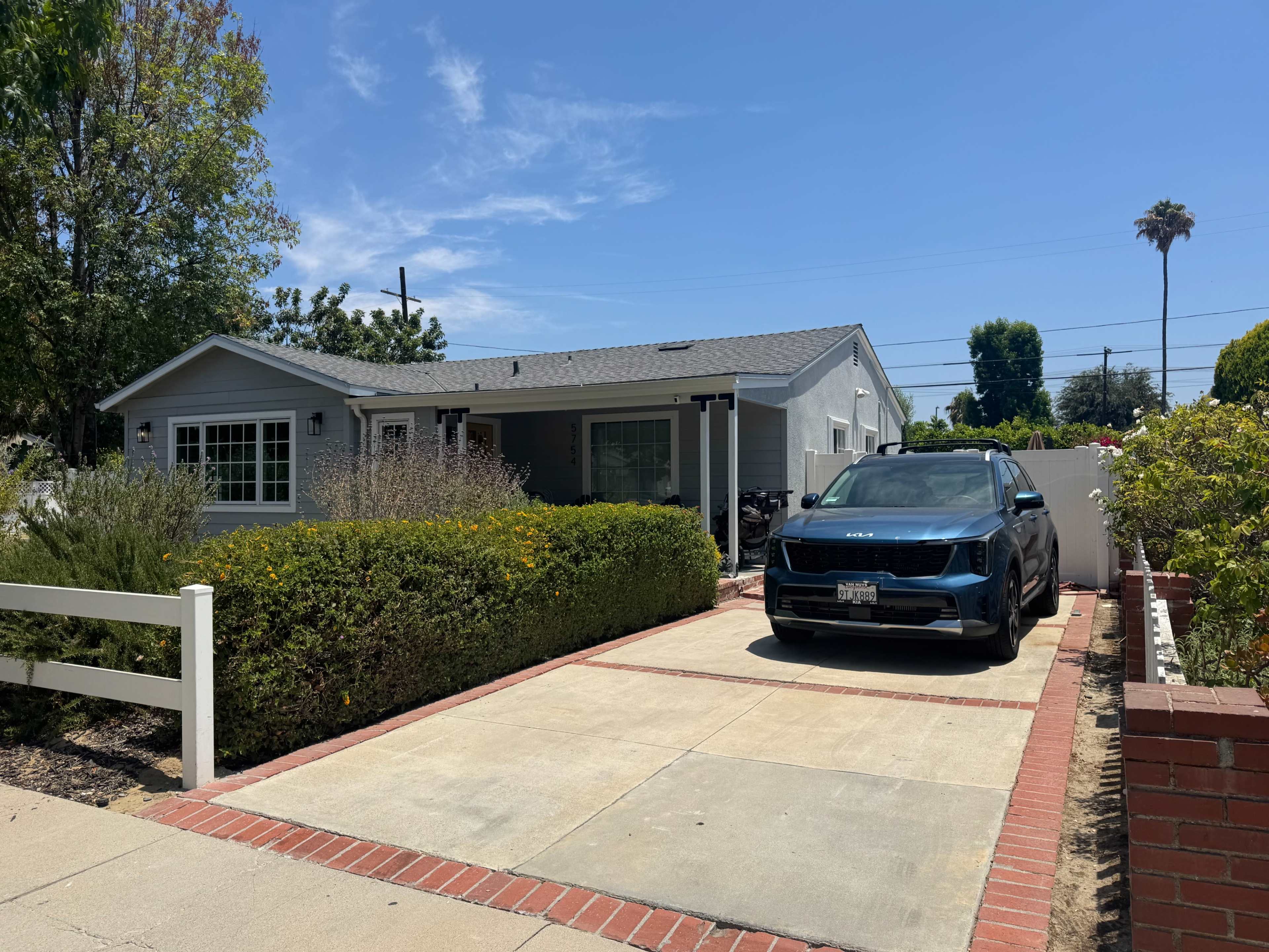 A single-story gray house with a front lawn, flower beds, and a black car parked in the driveway.