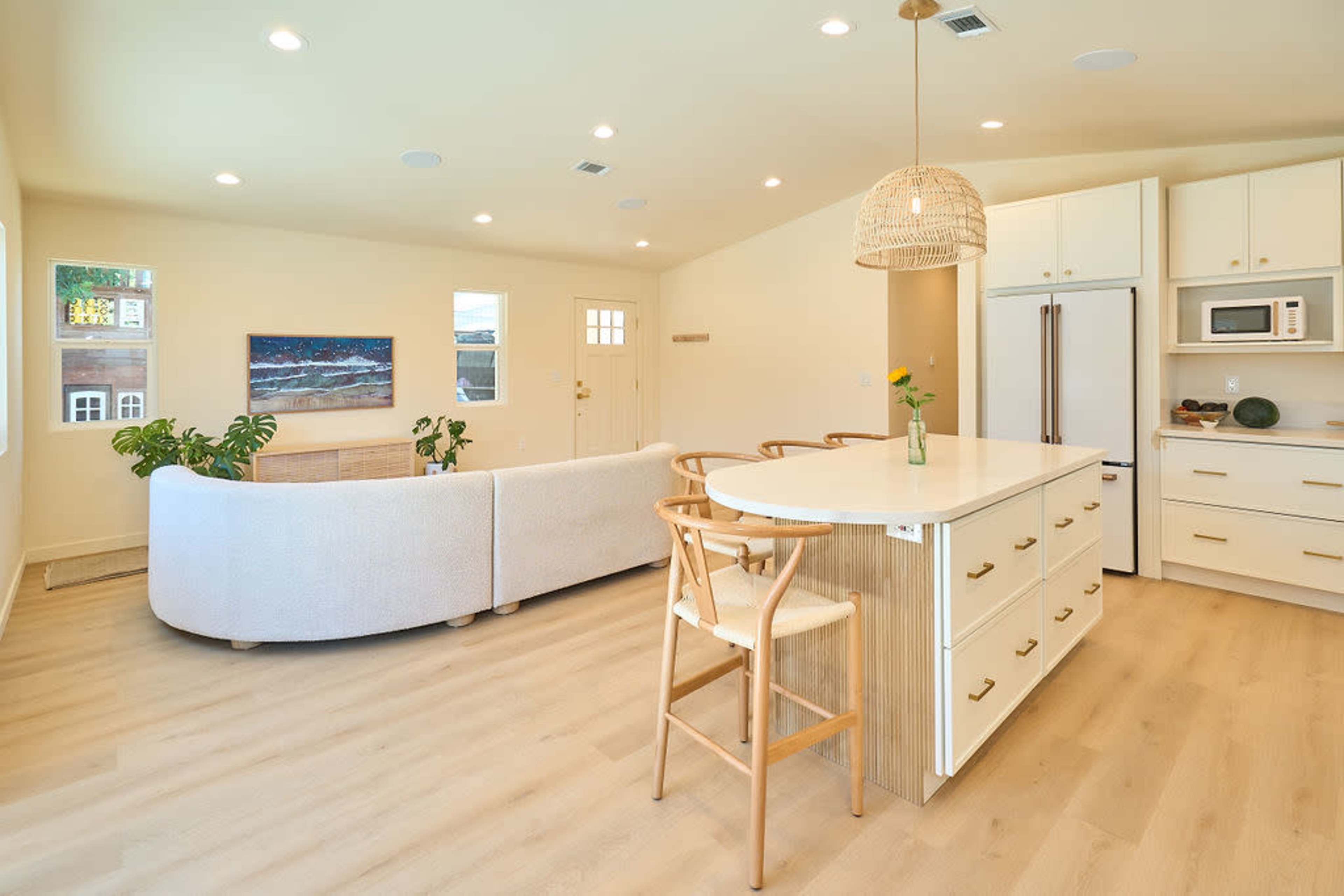 The image shows a bright, open-concept living space with a modern kitchen and a cozy seating area featuring a white sofa and minimalistic decor.