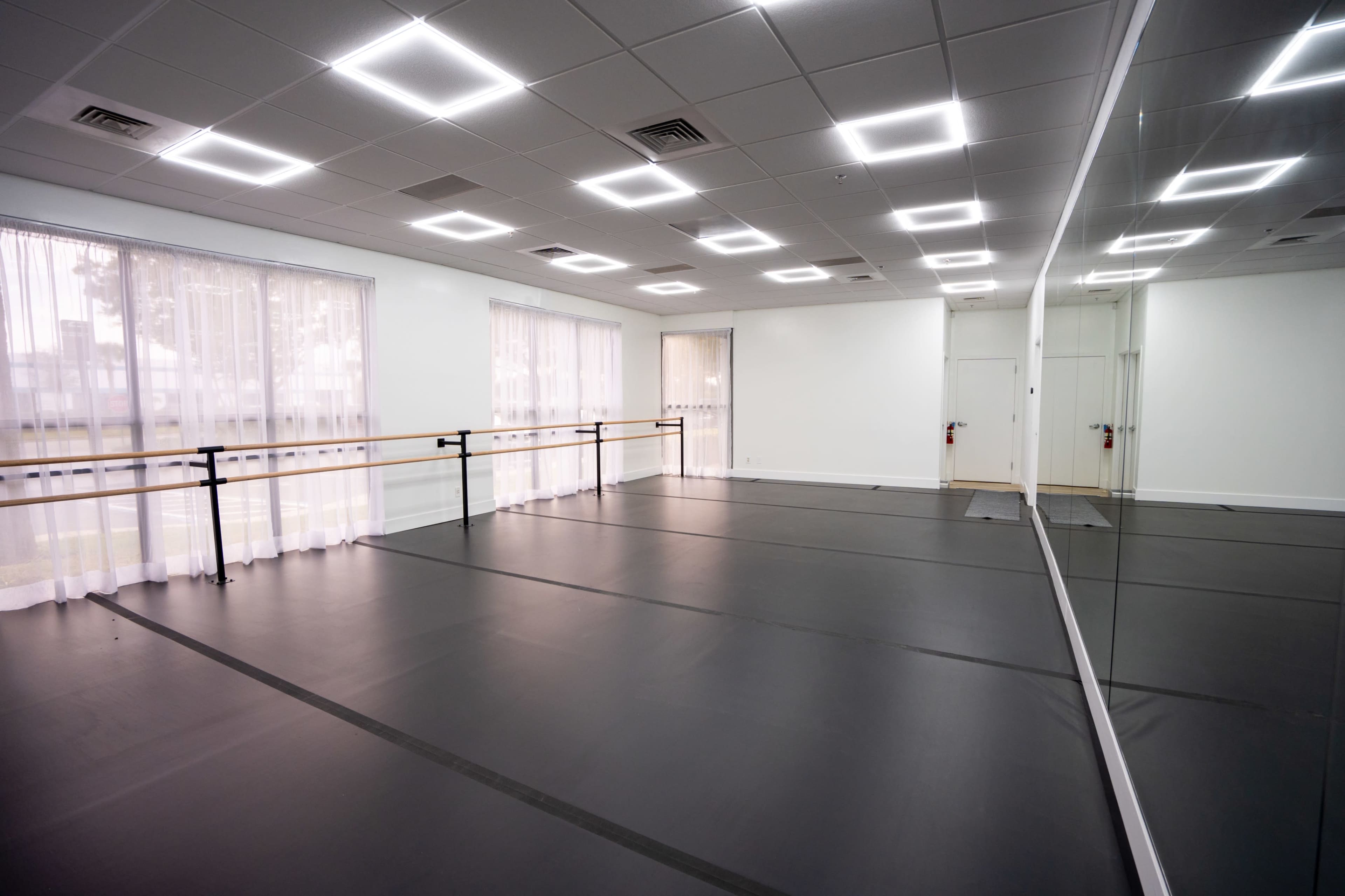 The image shows a spacious dance studio equipped with mirrors, a ballet barre, and black flooring.