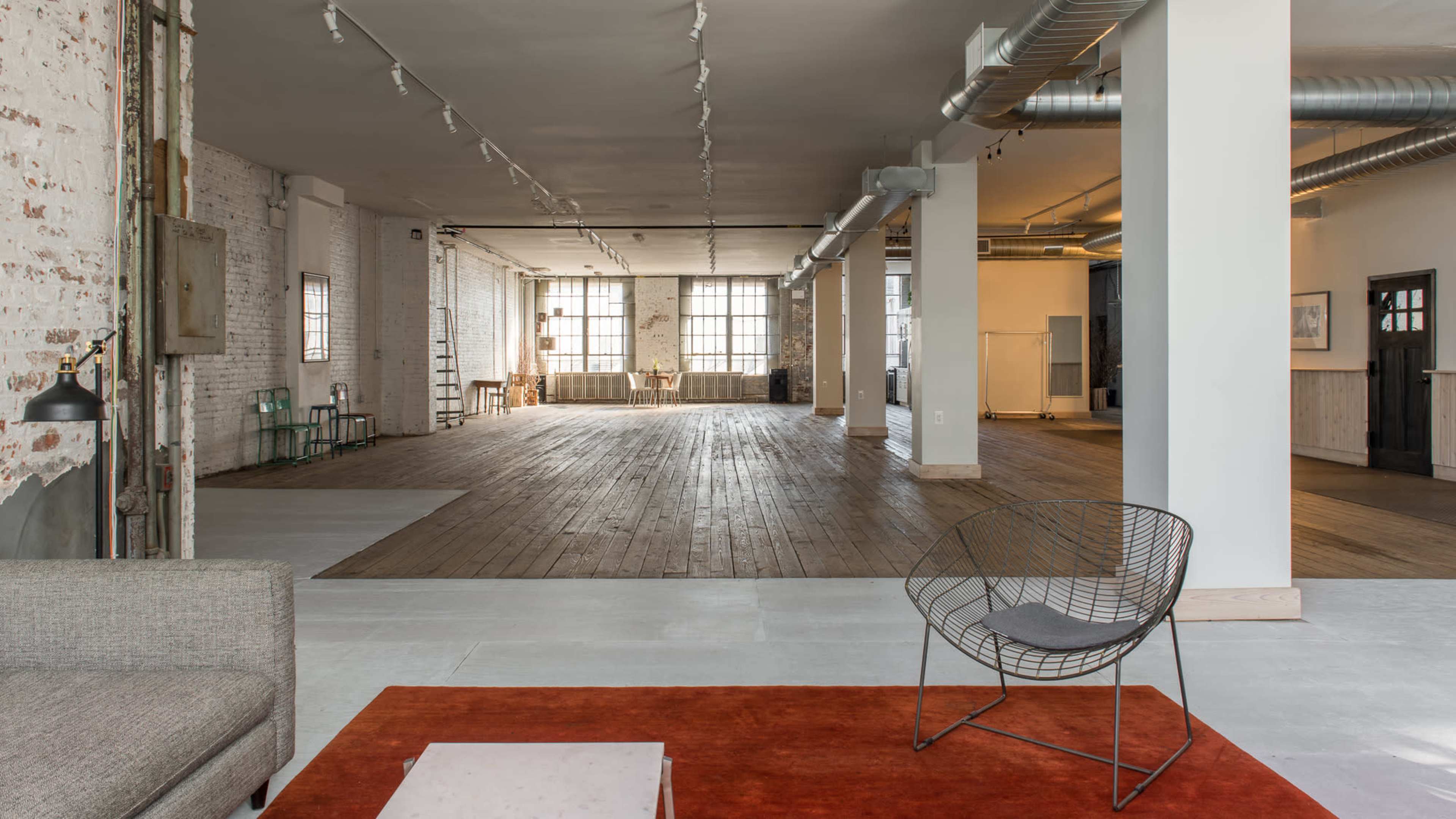 A spacious, open loft with exposed brick walls, wooden flooring, and large windows allowing ample natural light.