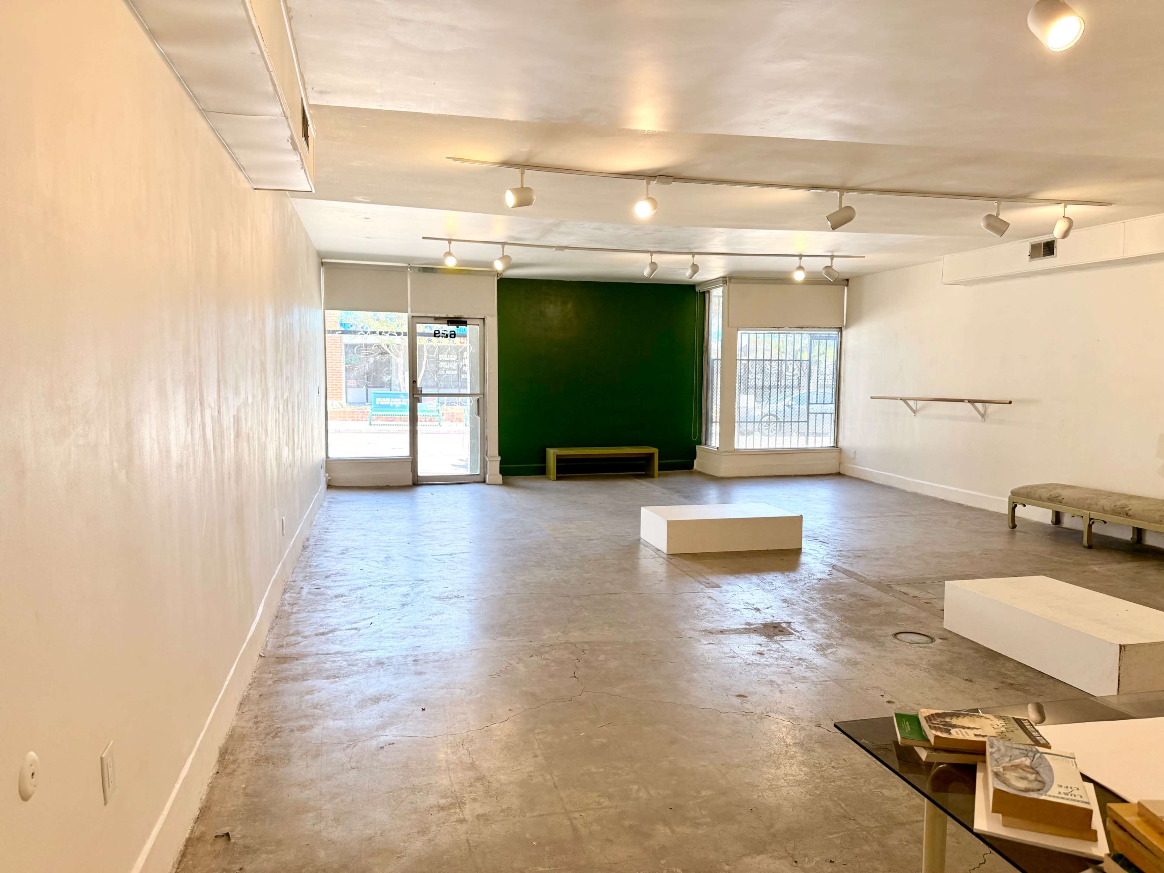 The image shows an empty, well-lit gallery space with a green accent wall and a few minimalist display pieces.