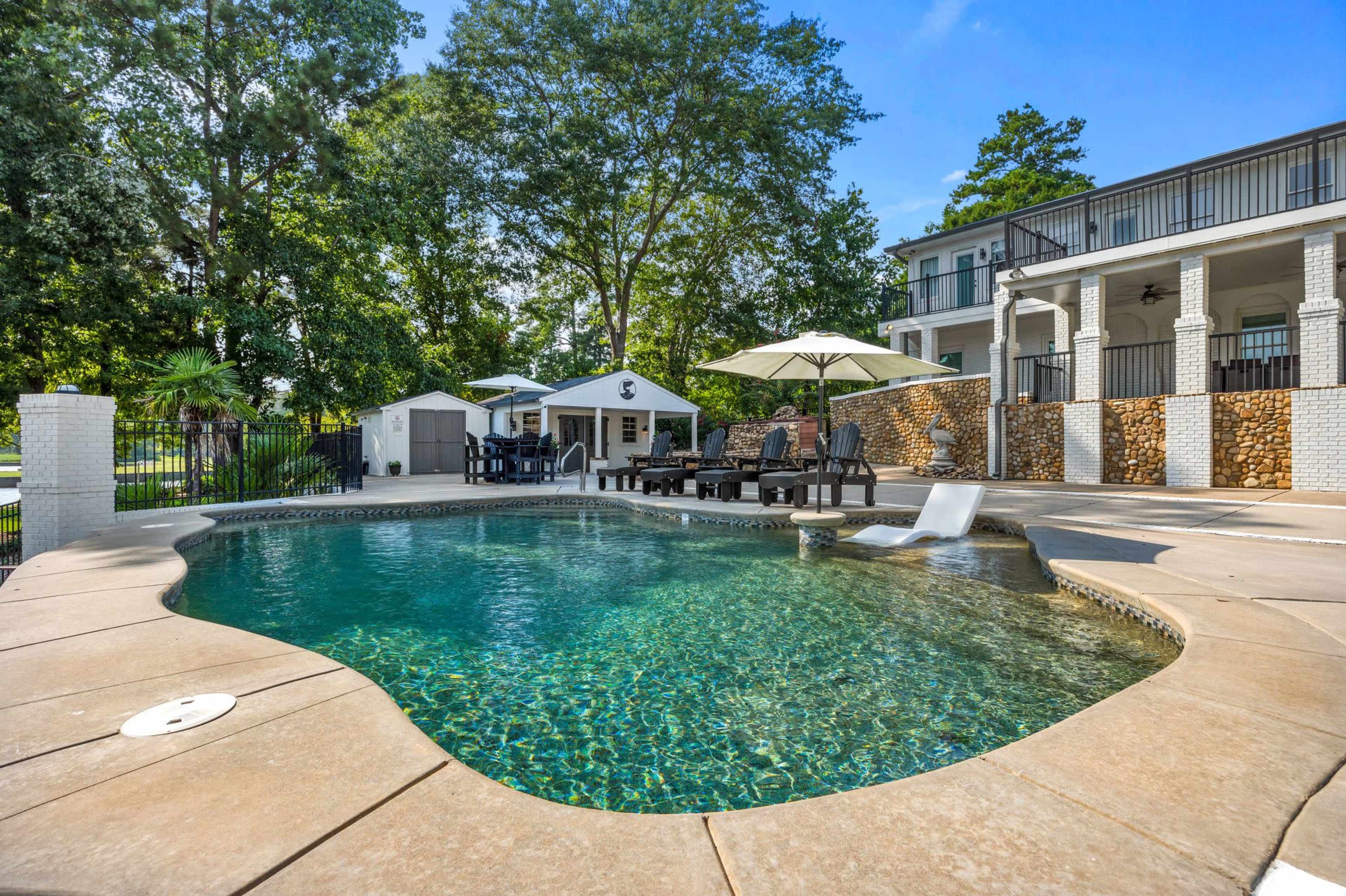 The image shows a residential backyard featuring a swimming pool with a lounge area, umbrellas, and a two-story house in the background.