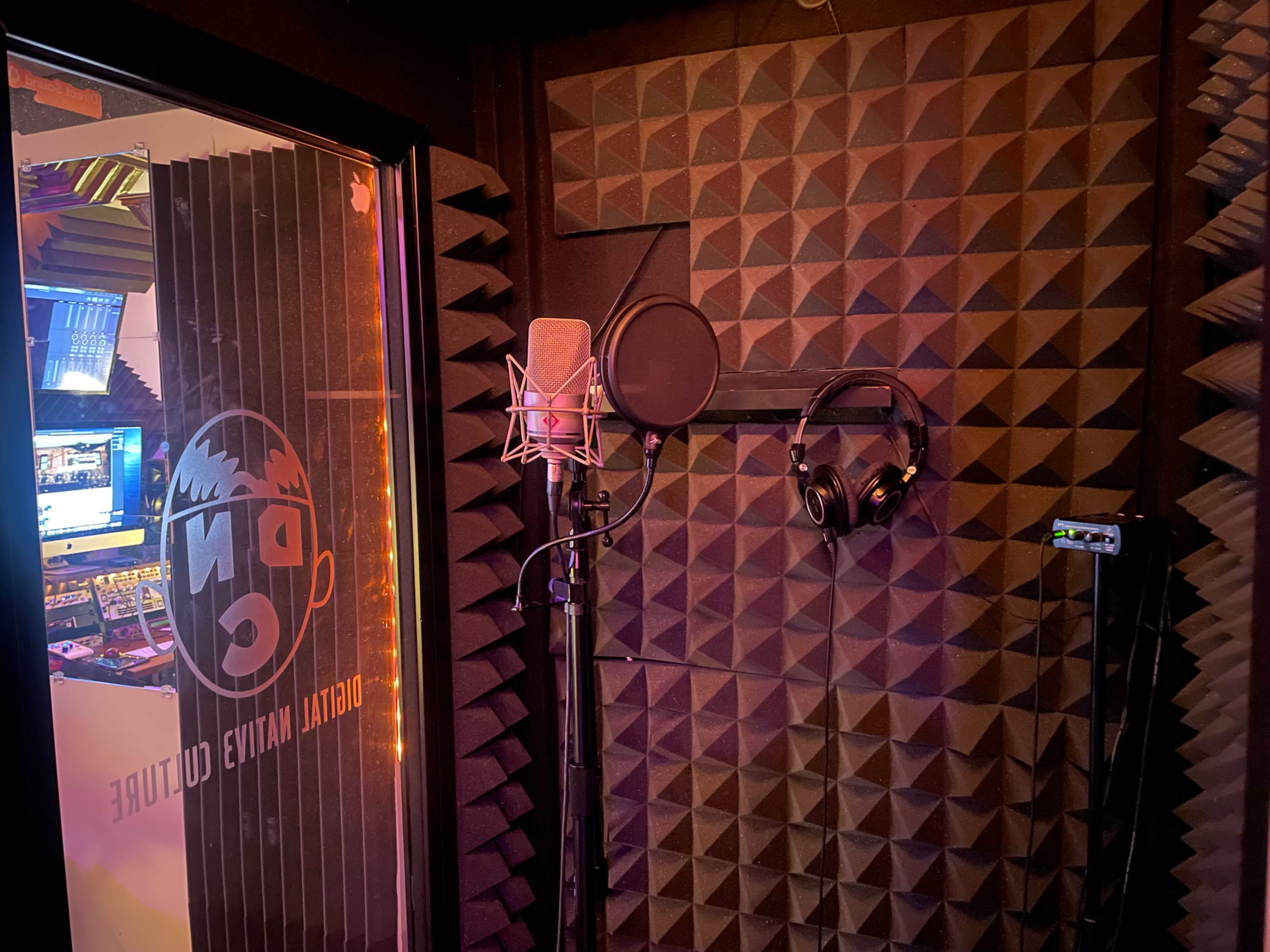 A recording booth with soundproof walls, a microphone on a stand, and headphones hanging nearby.