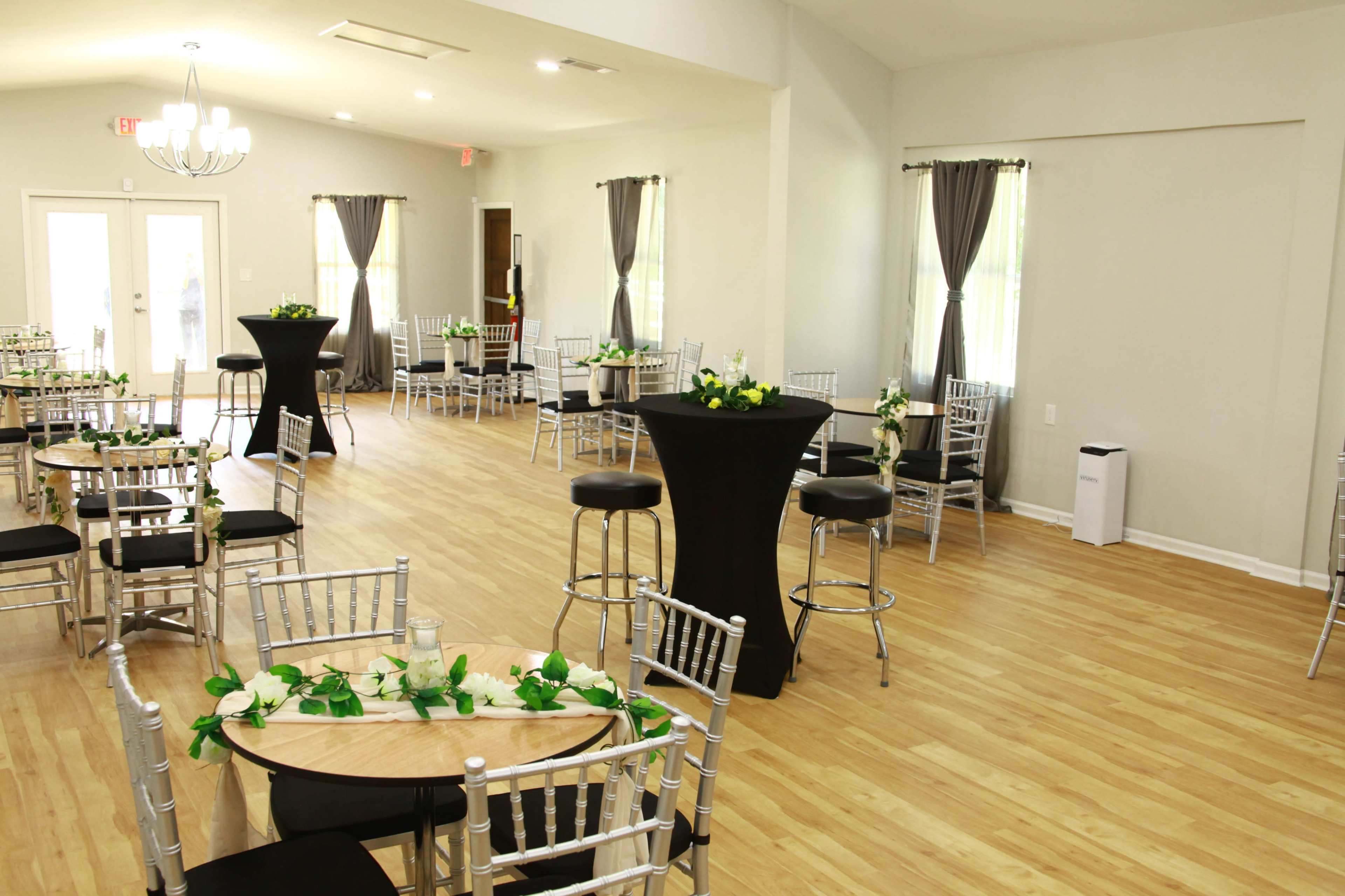 A spacious event room with silver chiavari chairs, black cocktail tables, and floral decorations on the tables.