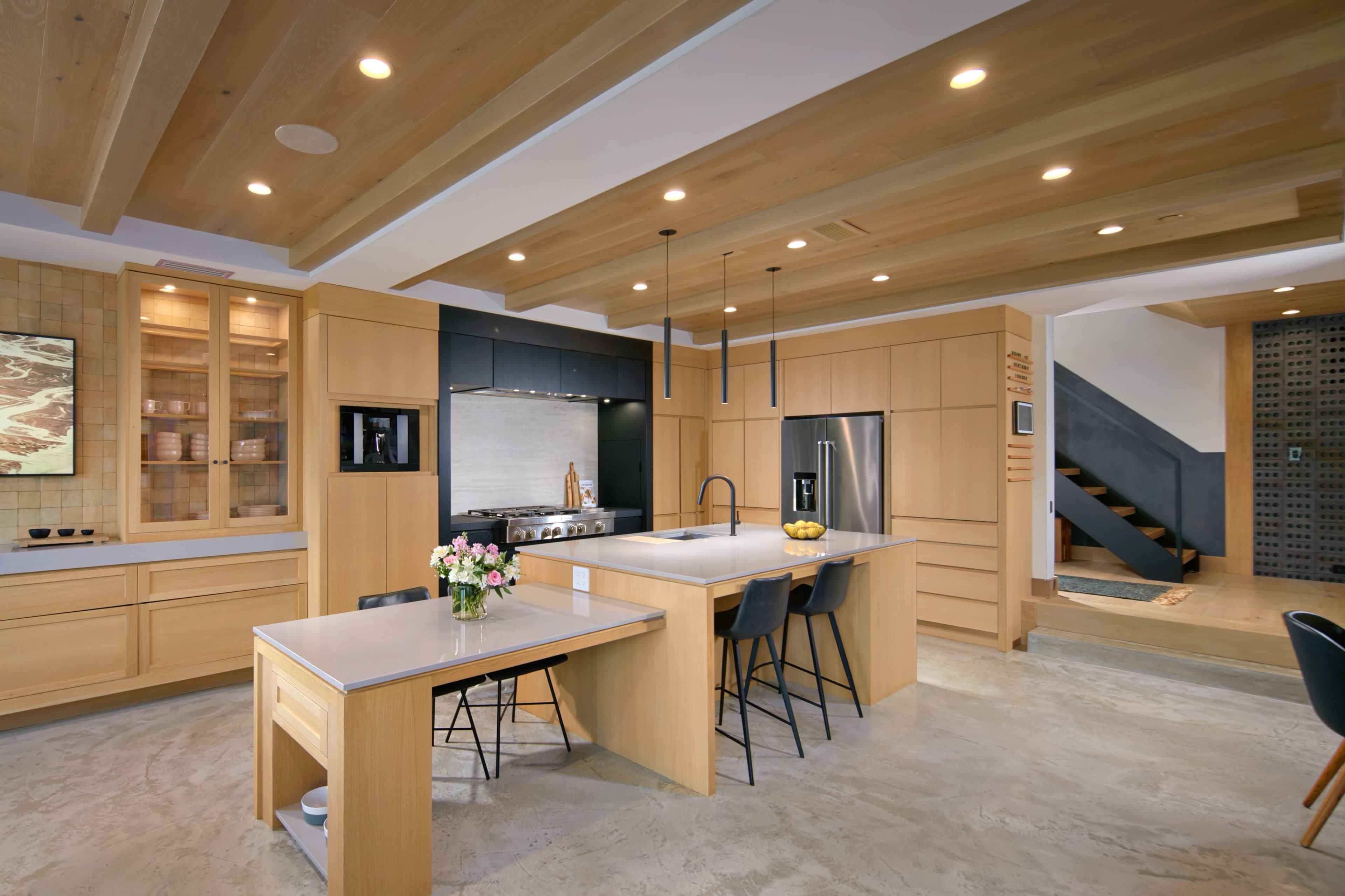 A modern kitchen with wooden cabinetry, a central island, and sleek appliances, featuring a mix of light wood and gray surfaces.
