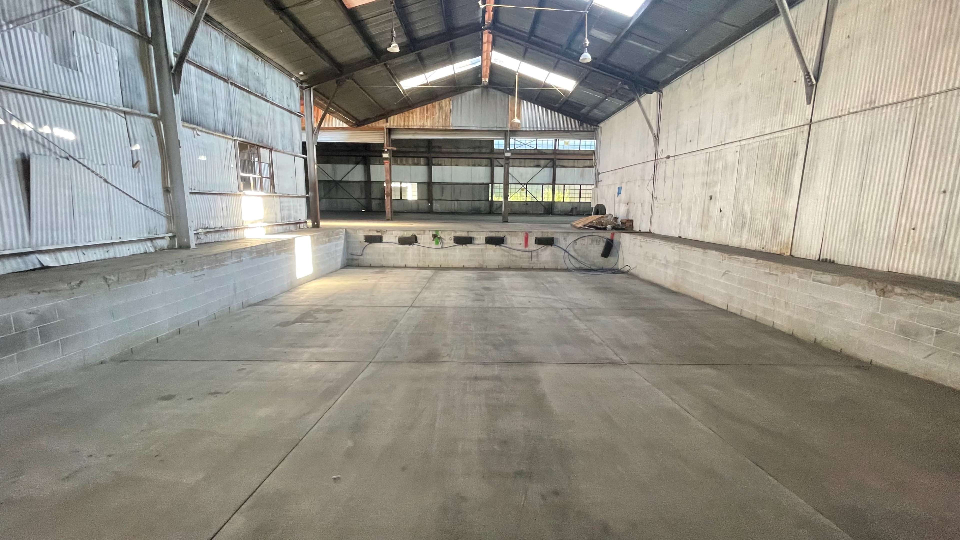 An empty industrial warehouse with a concrete floor, steel beams, and large open spaces.