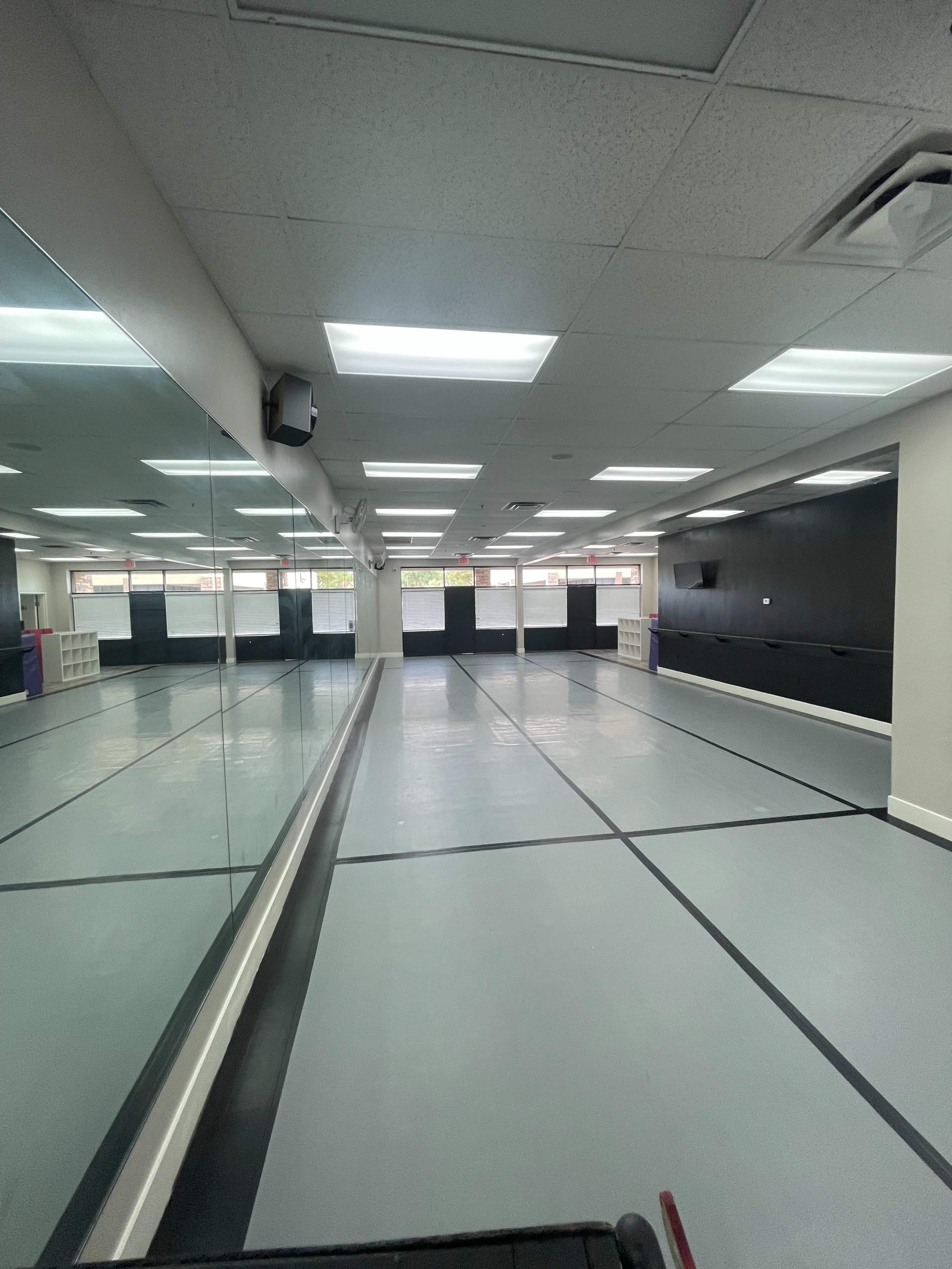 An empty dance studio with mirrored walls and fluorescent lighting.
