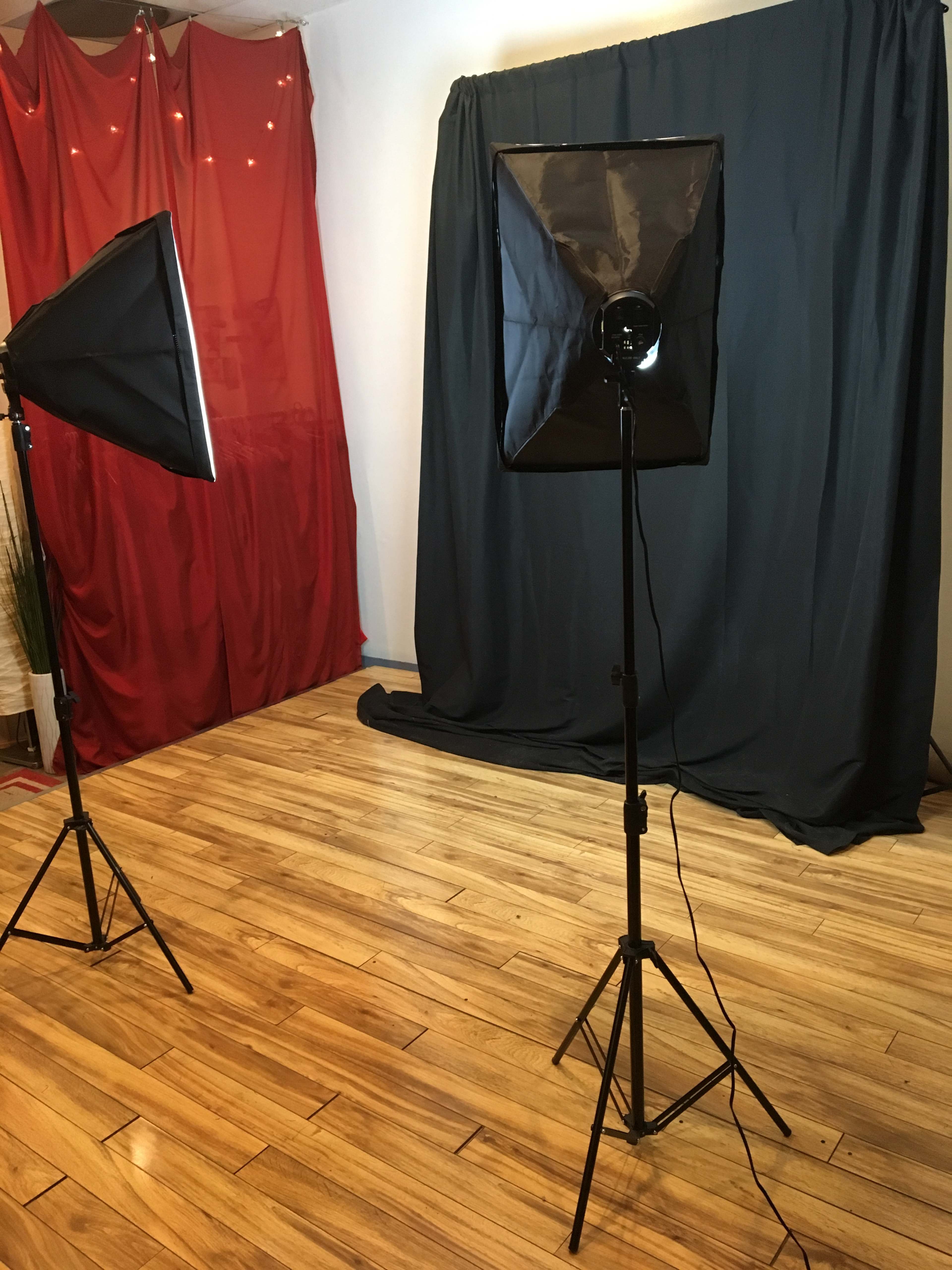 A photography studio setup with two softbox lights positioned in front of a black backdrop, and a red curtain to one side on a wooden floor.