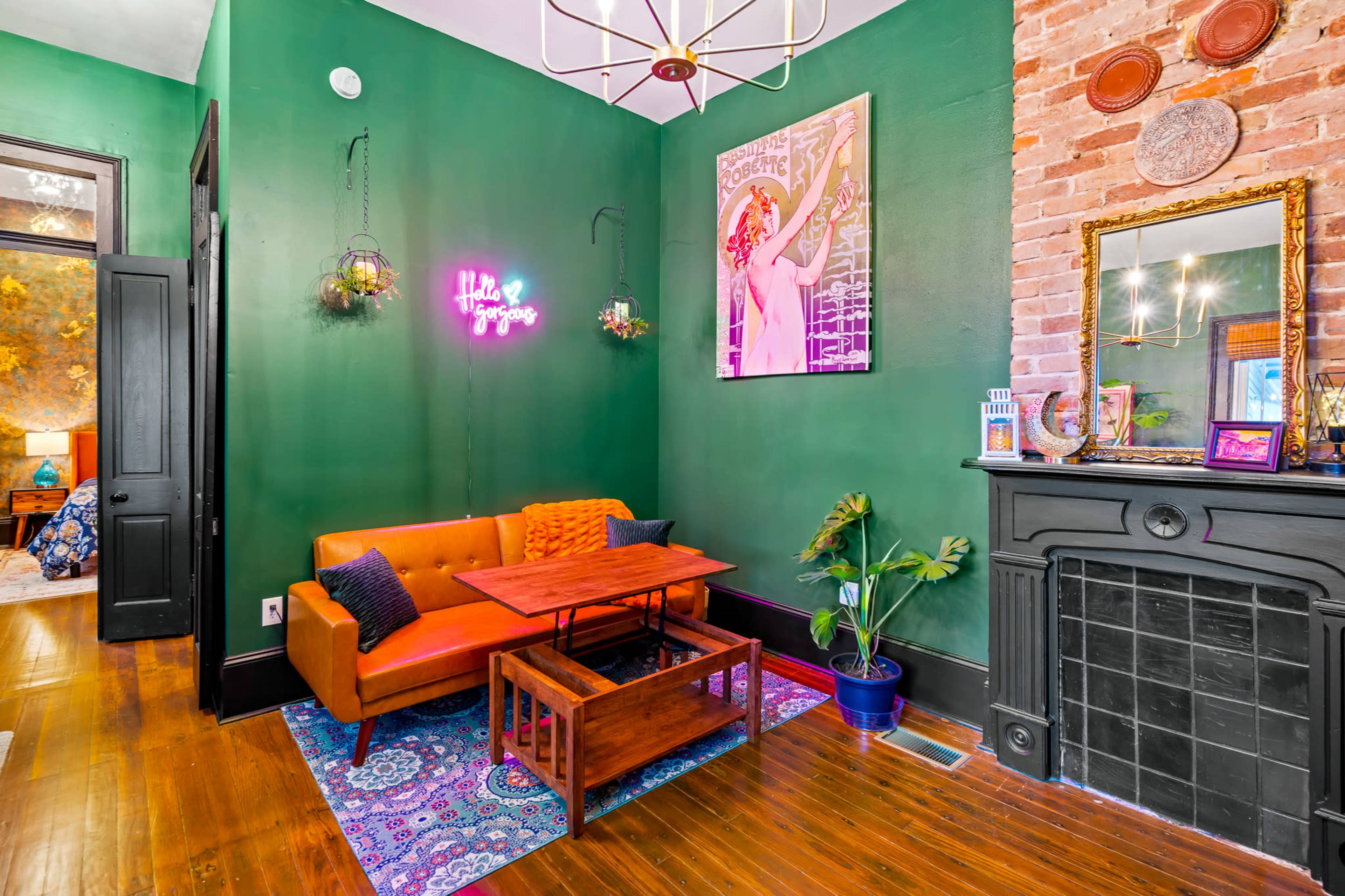 The image shows a room with green walls, featuring an orange couch, a wooden coffee table, and decorative plants near a fireplace.