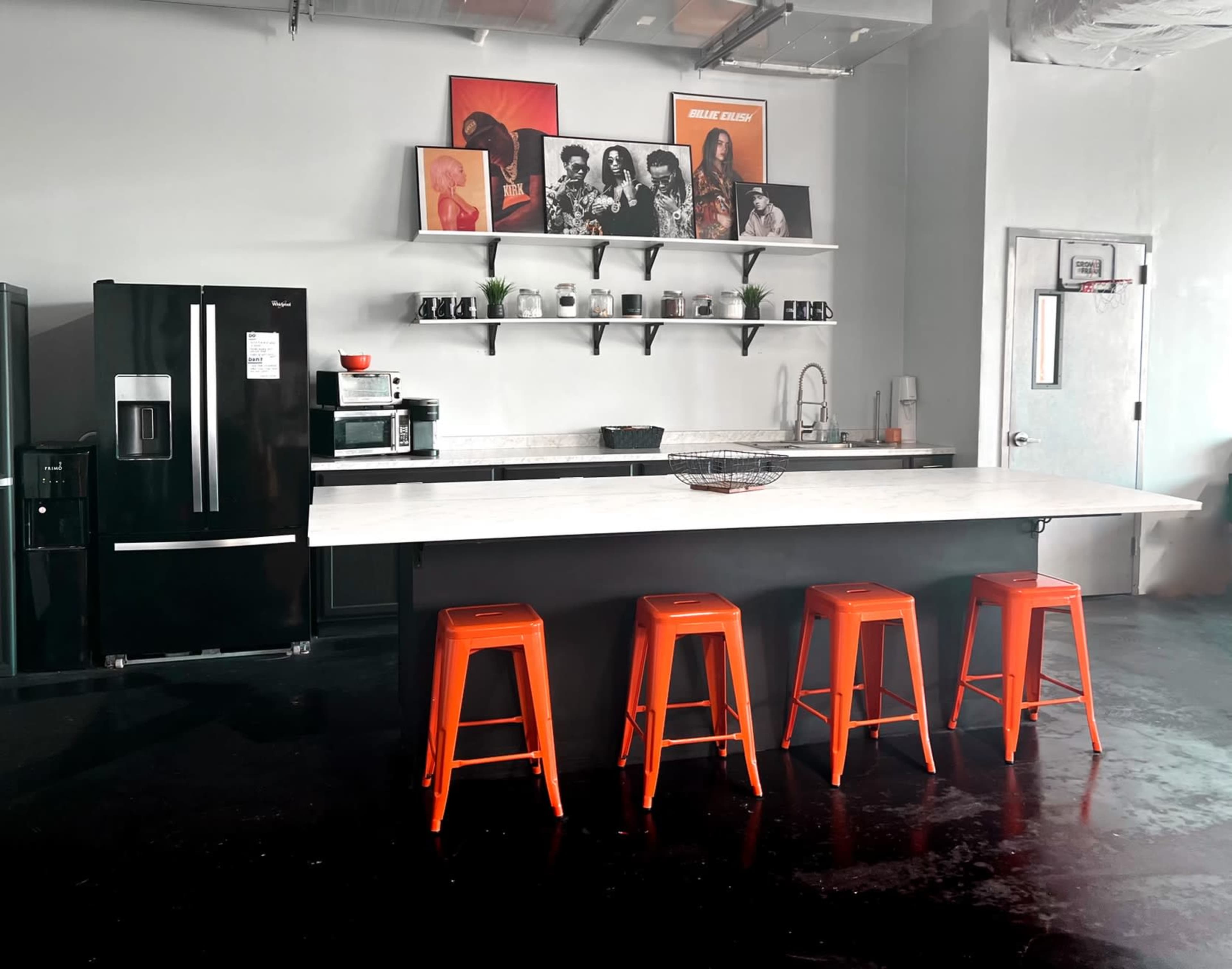 A modern kitchen with a marble island, four orange stools, a black refrigerator, and decorative artwork on the walls.