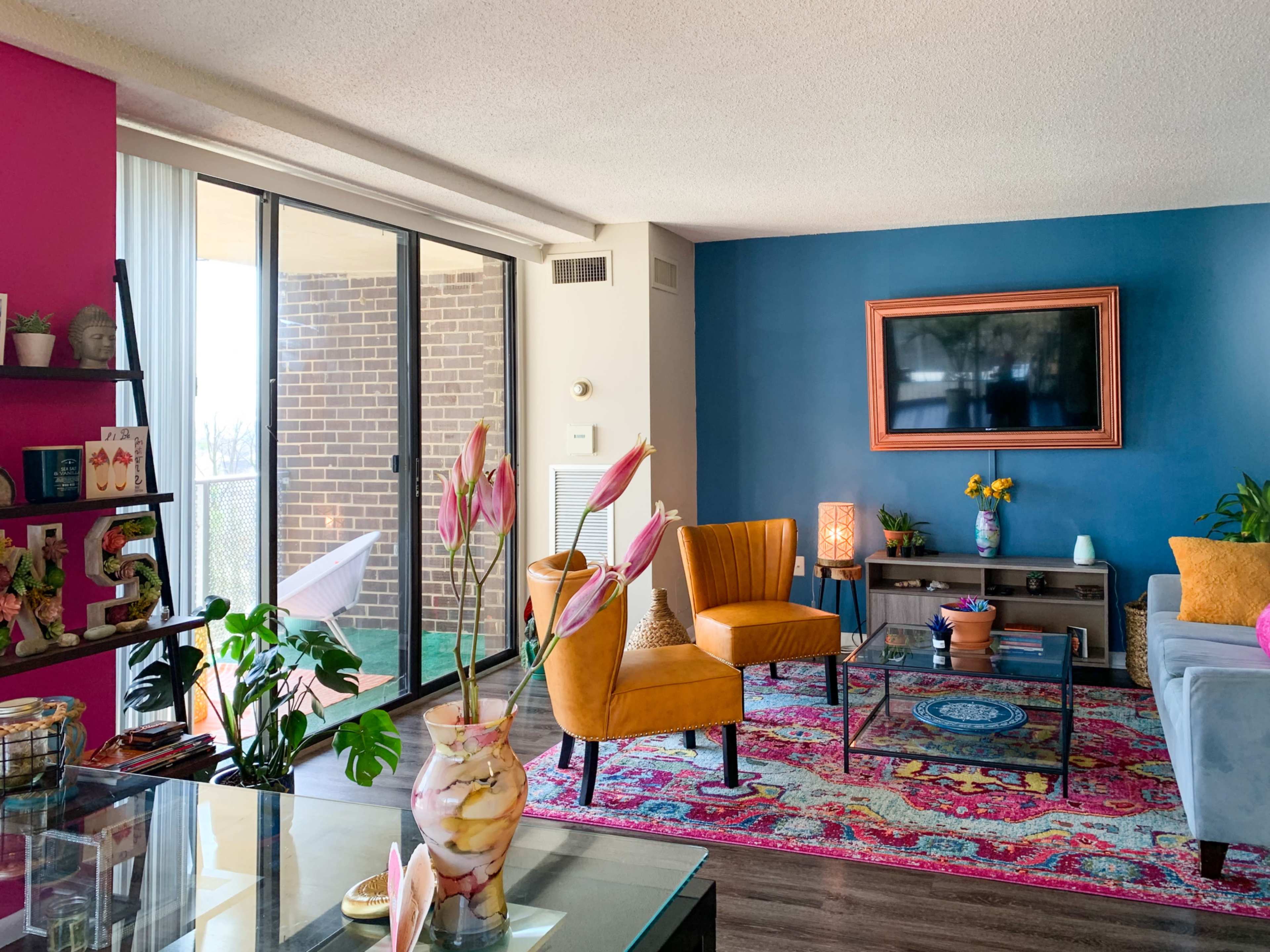 A colorful living room features a blue accent wall, a flat-screen TV, orange chairs, and a patterned rug.