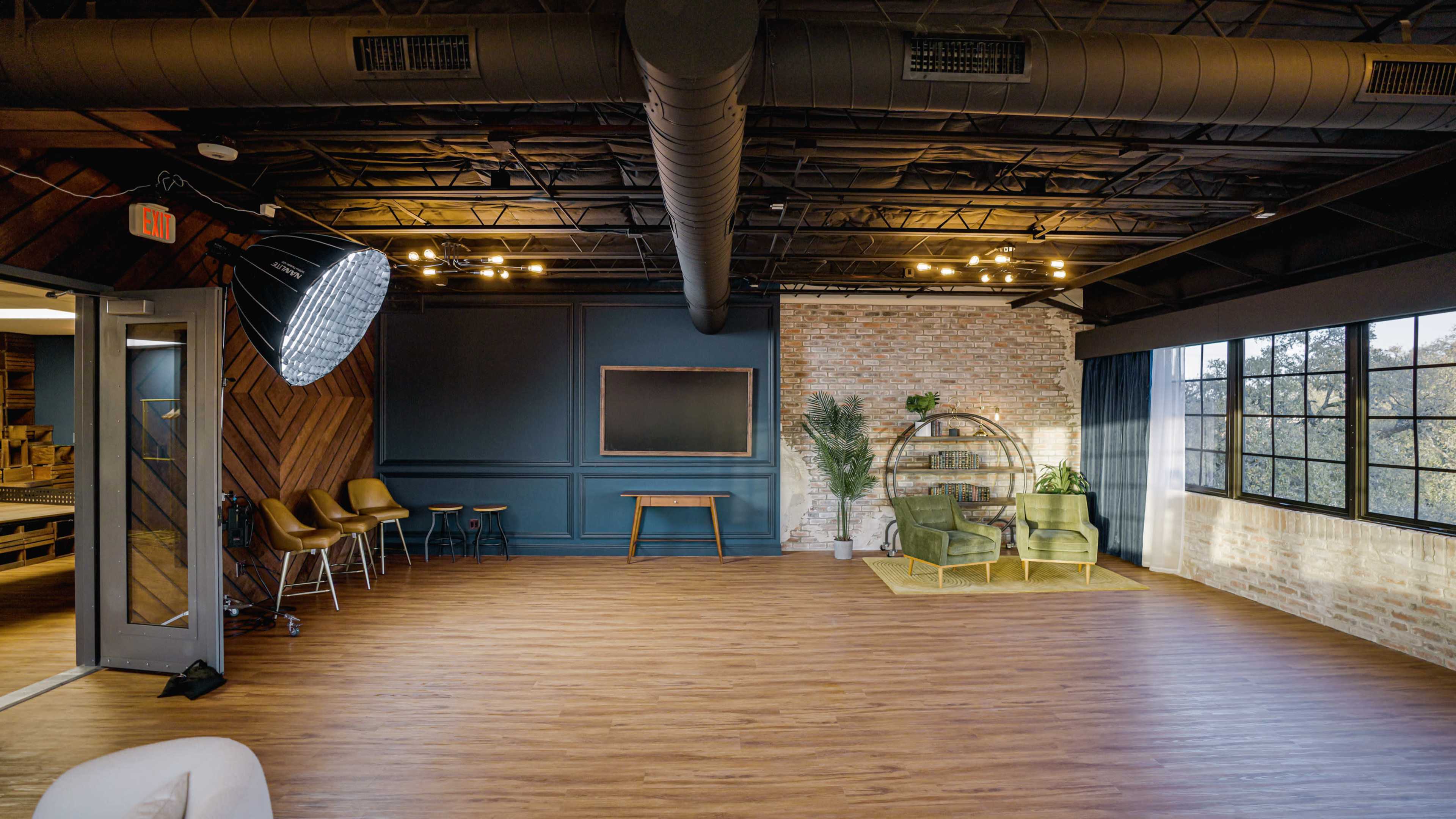 The image shows a modern, spacious interior with wooden flooring, a large window, a green sofa set, and a decorative wall.