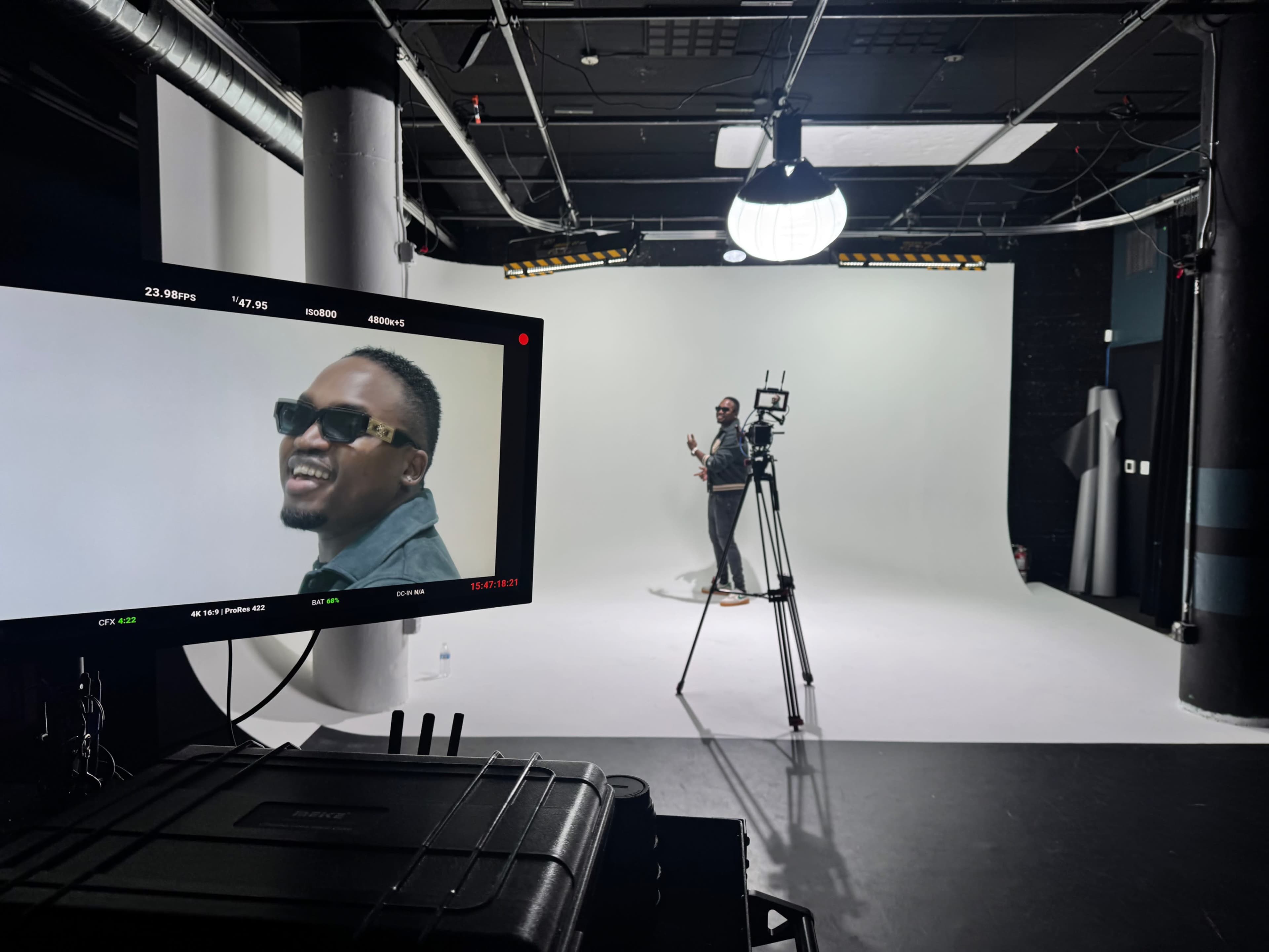 A camera setup captures a subject performing in front of a plain white backdrop in a studio.