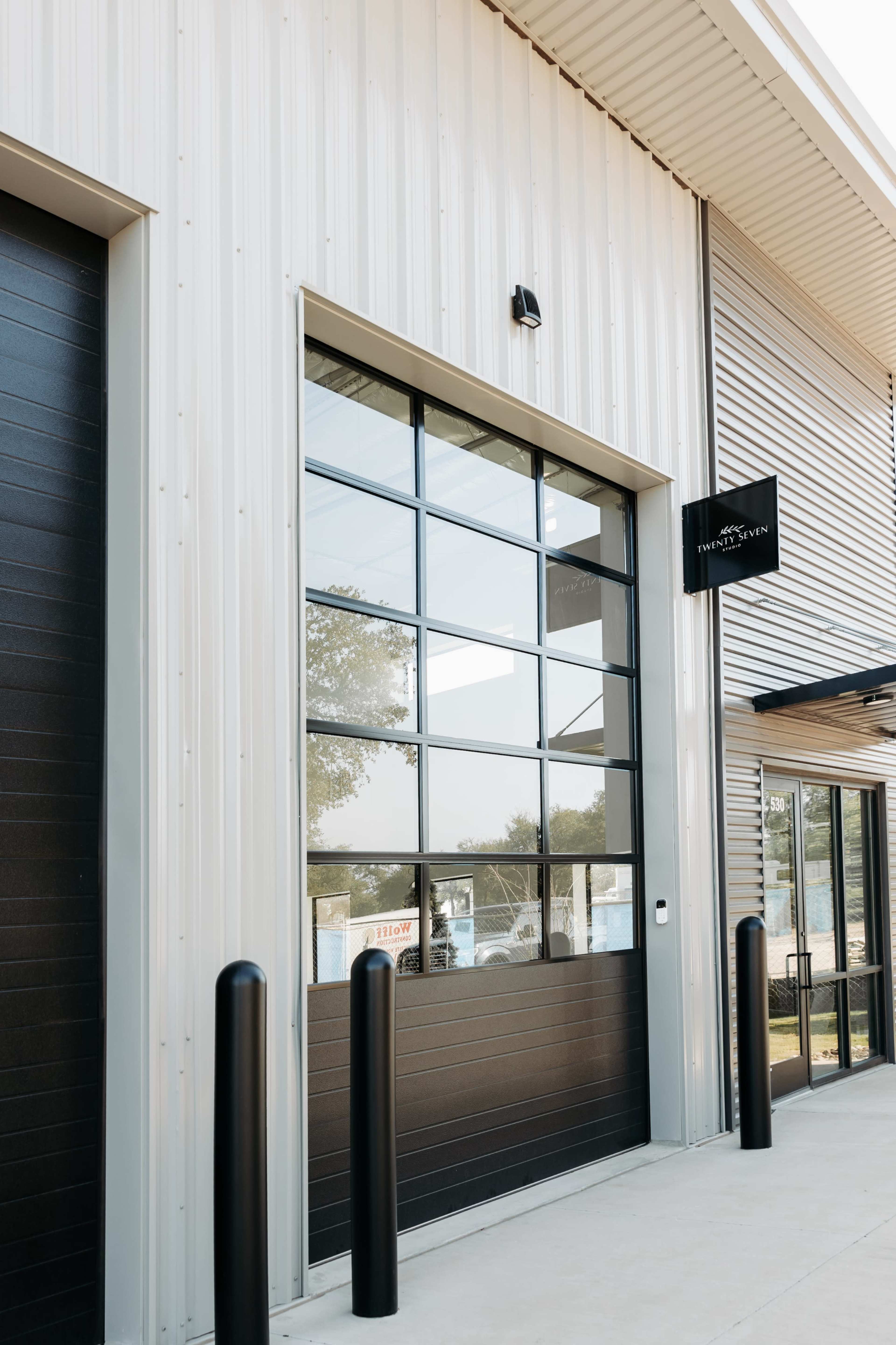 The image shows a modern building exterior featuring large glass panel doors and a sign mounted above the entrance.