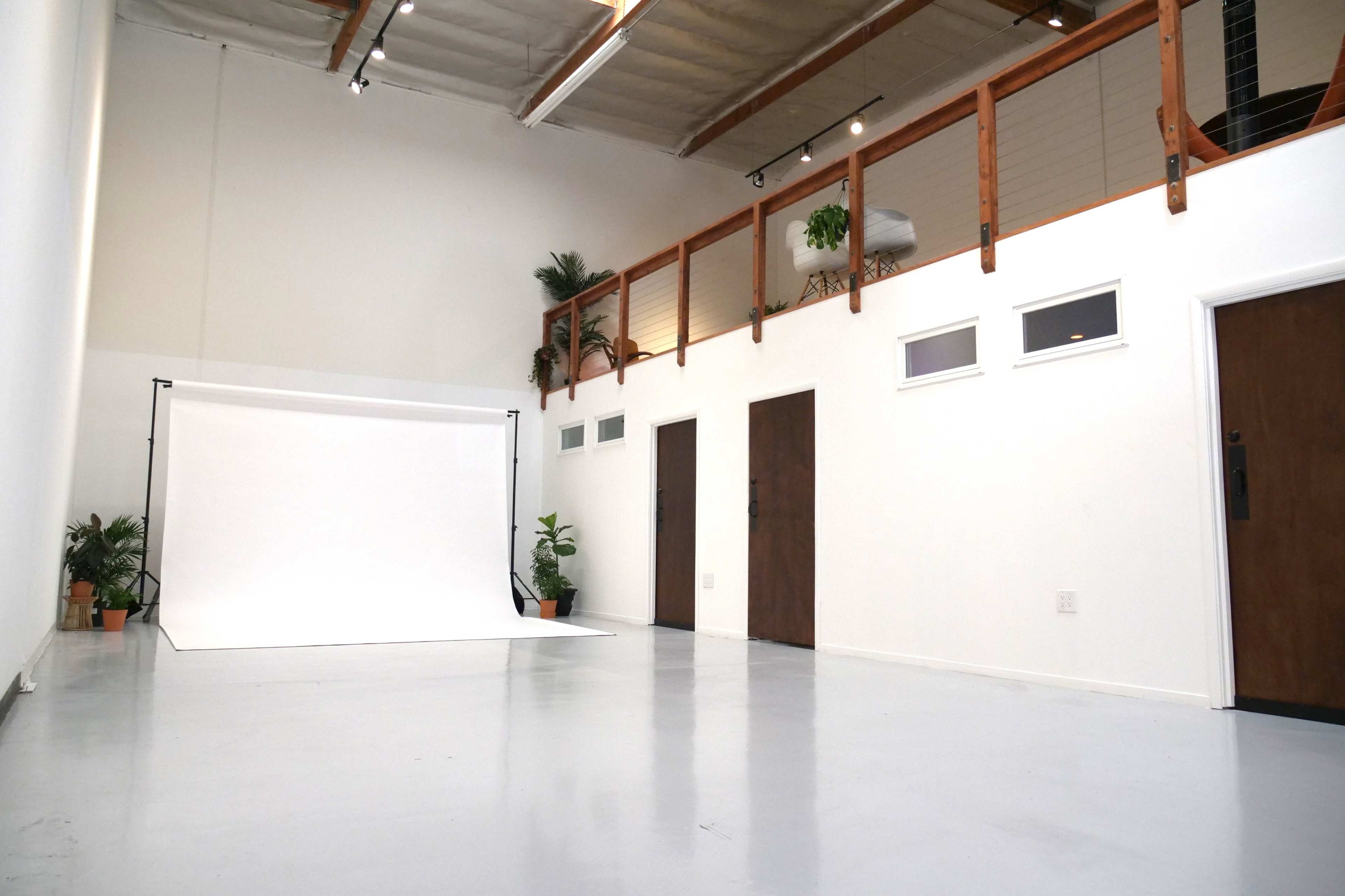 A spacious, minimalist studio with a white backdrop, wooden accents, and several doors leading to other areas.