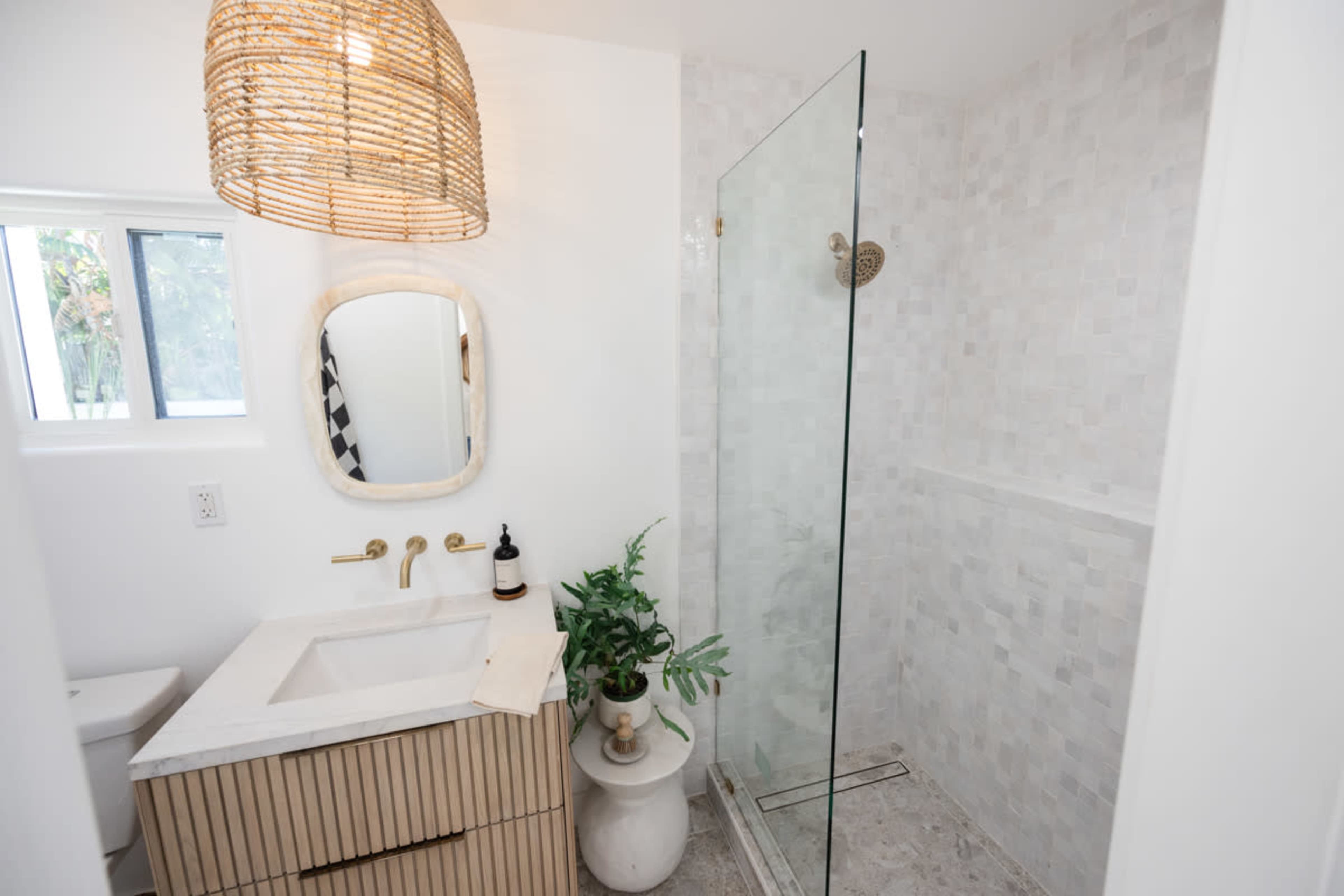 A modern bathroom with a glass shower, a wooden vanity with a marble countertop, and a potted plant beside the vanity.