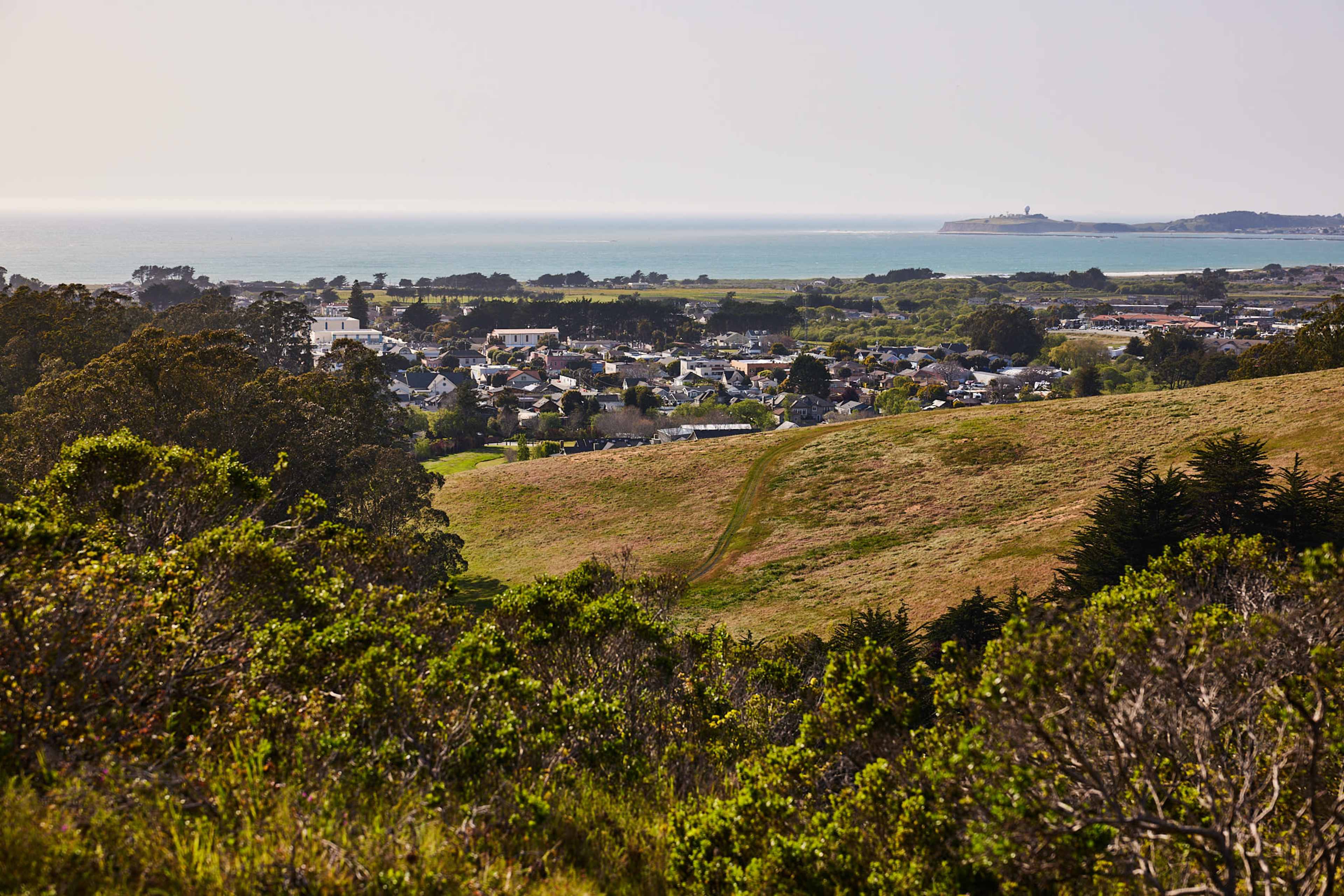 A coastal view with a small town nestled among green hills and the ocean in the background.
