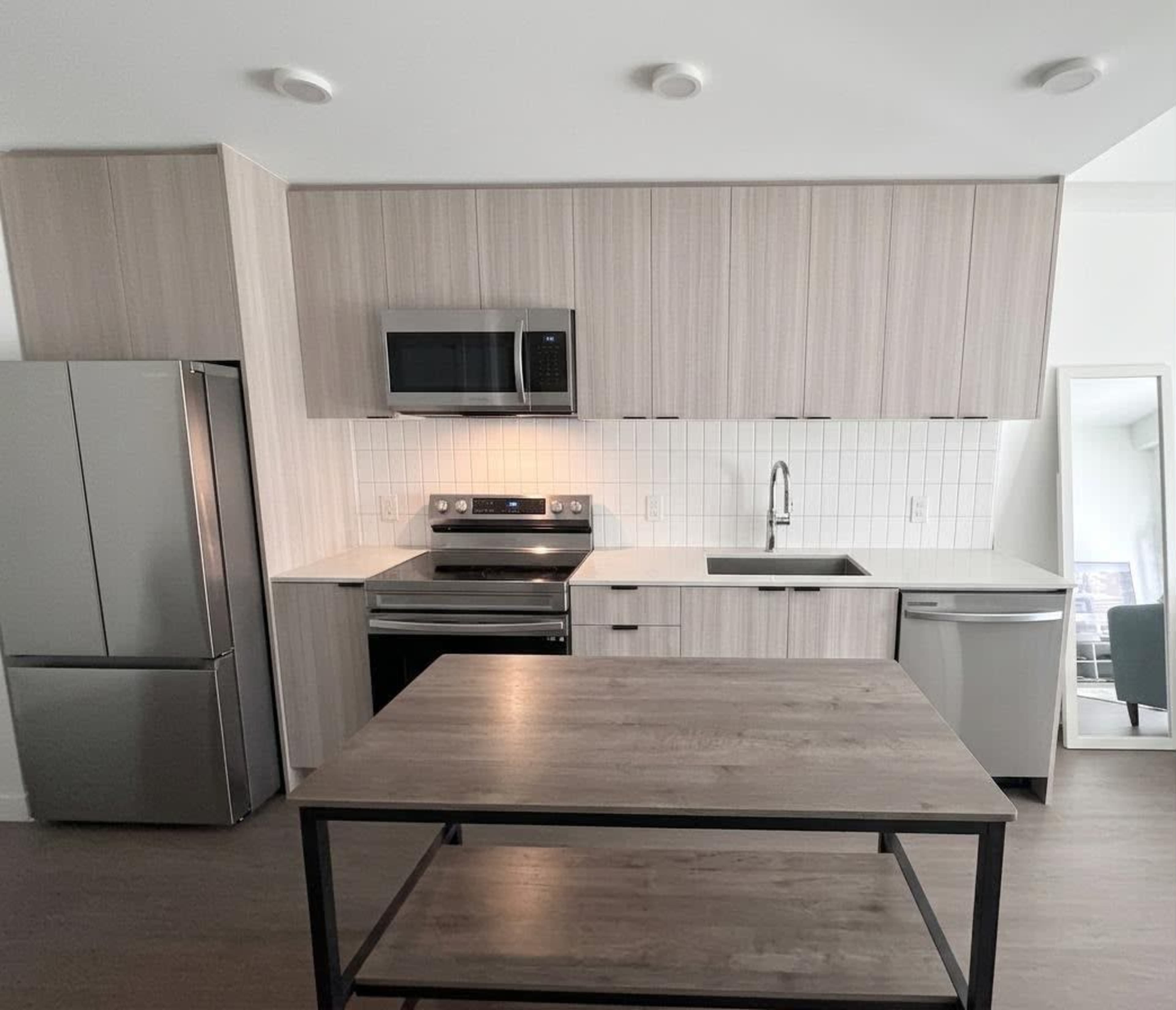 The image shows a modern kitchen featuring light wood cabinetry, stainless steel appliances, and a central island with a wooden top.