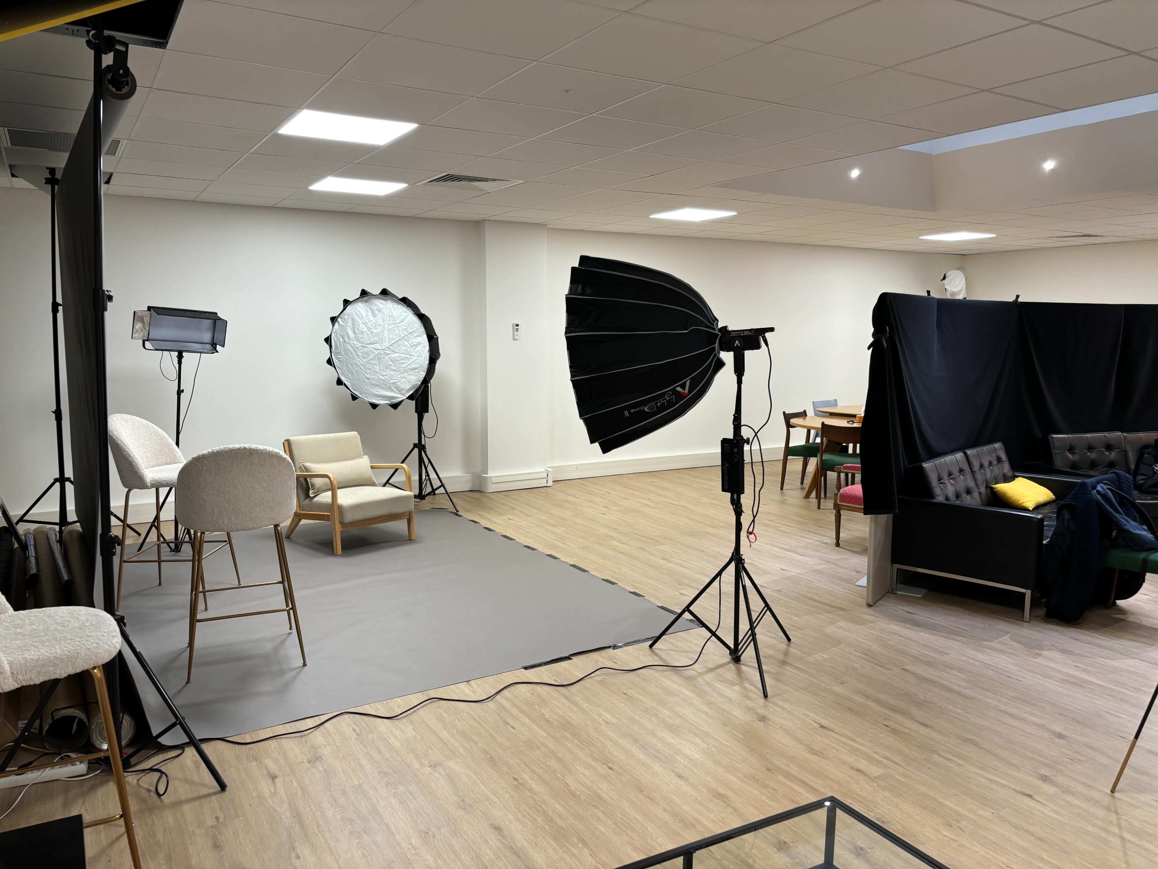 A well-lit studio setup featuring a seating area with chairs, lighting equipment, and a backdrop screen in a spacious room.