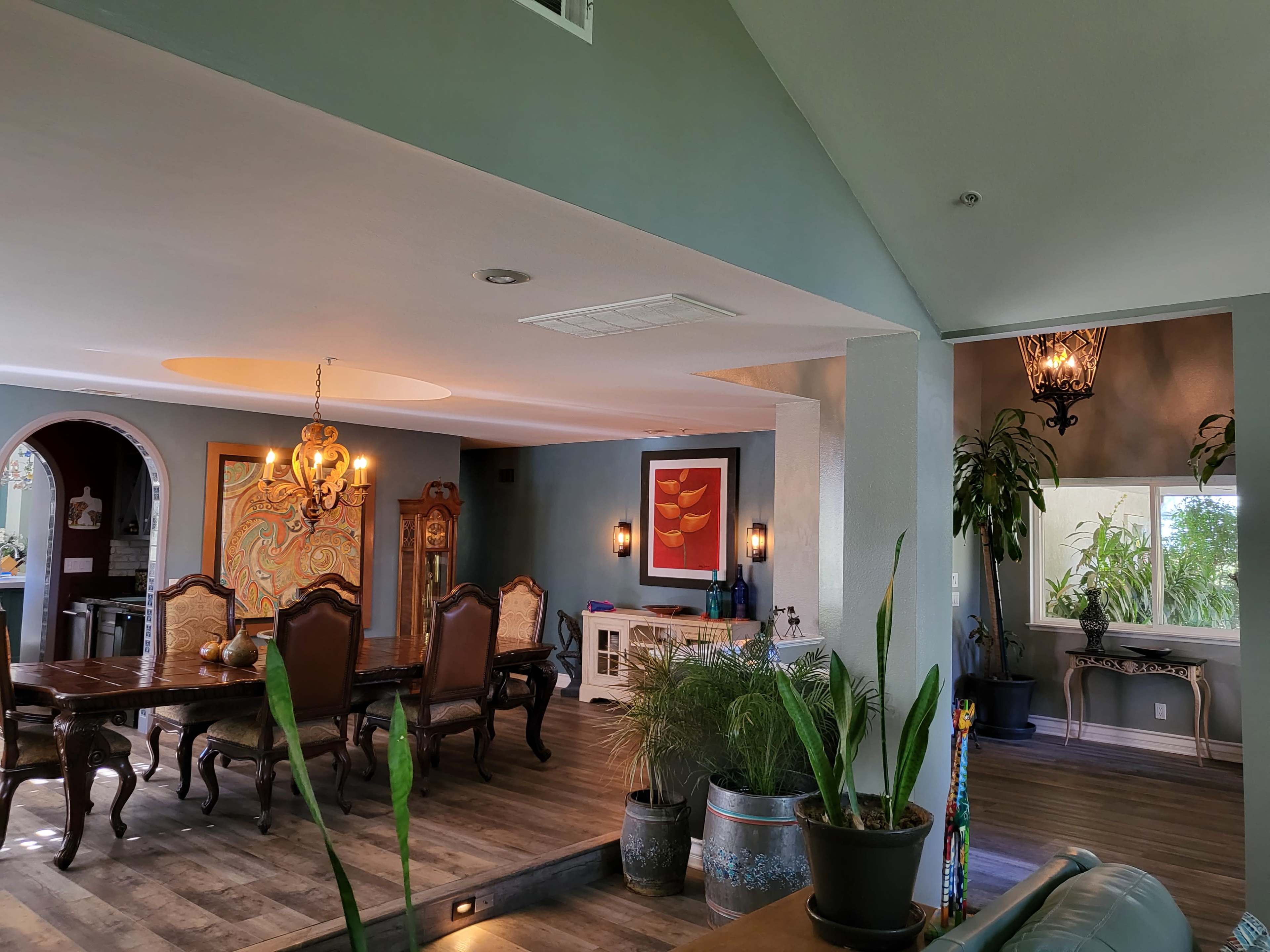An open living and dining area with wooden furniture, decorative plants, and a mix of wall art.