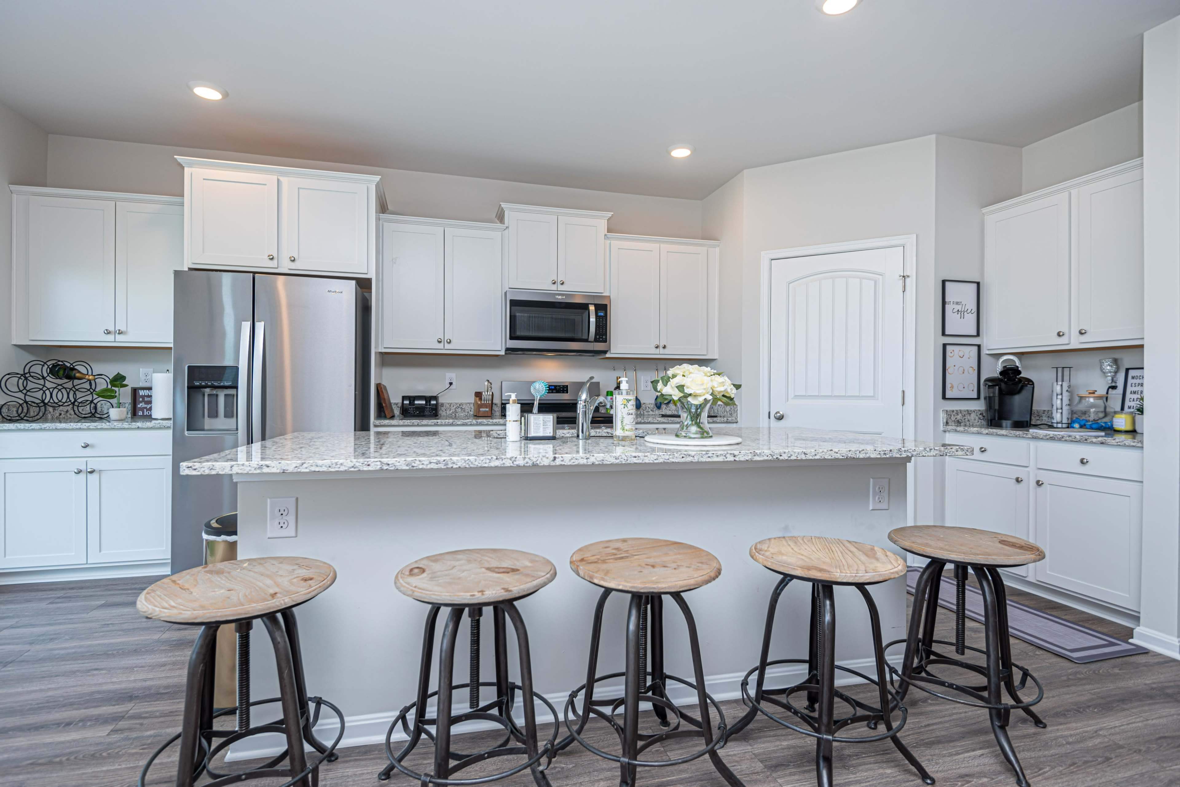 A modern kitchen features white cabinetry, stainless steel appliances, and a granite island with five wooden bar stools.