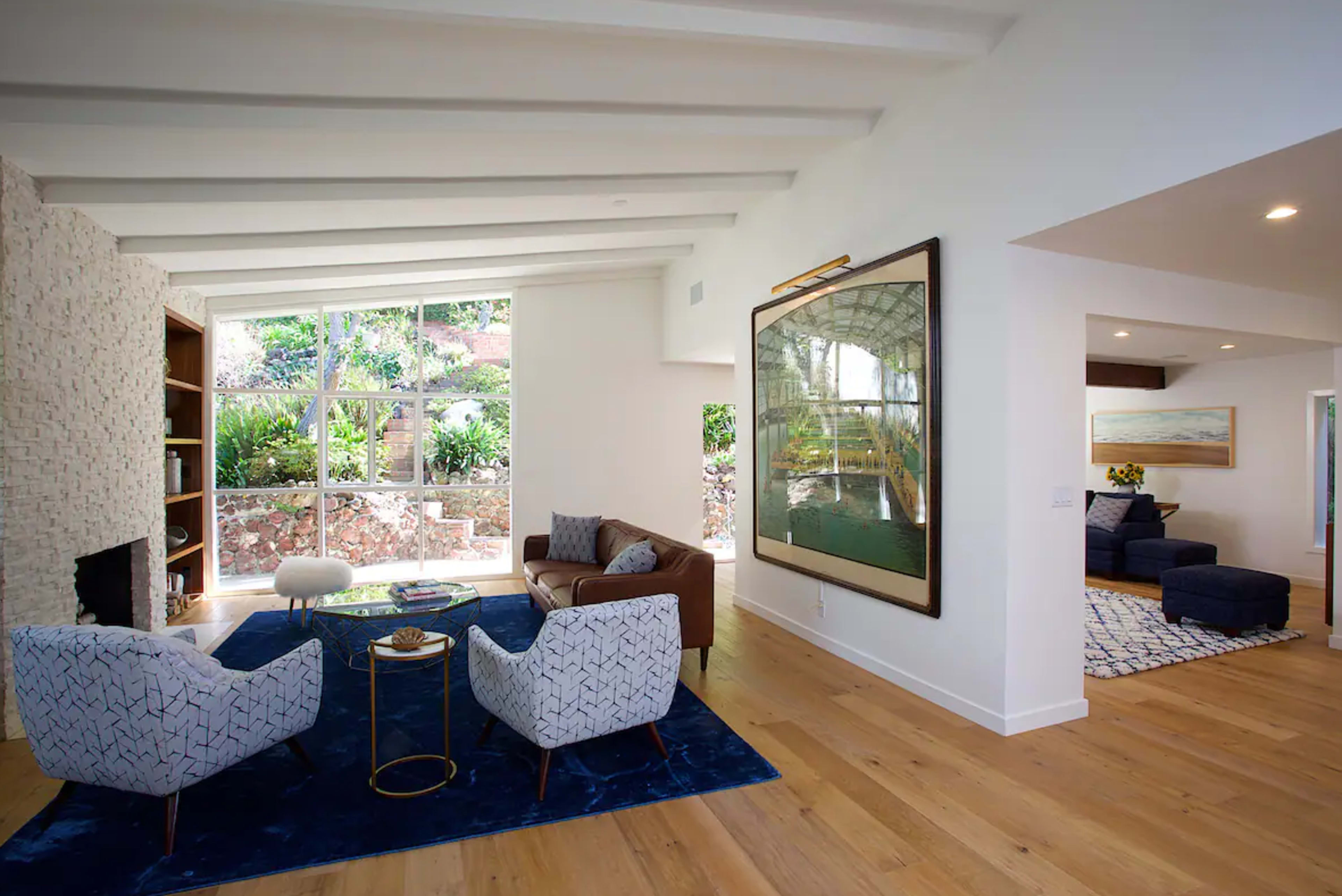 A modern living room with a sofa, armchairs, a coffee table, and large windows showcasing a garden outside.