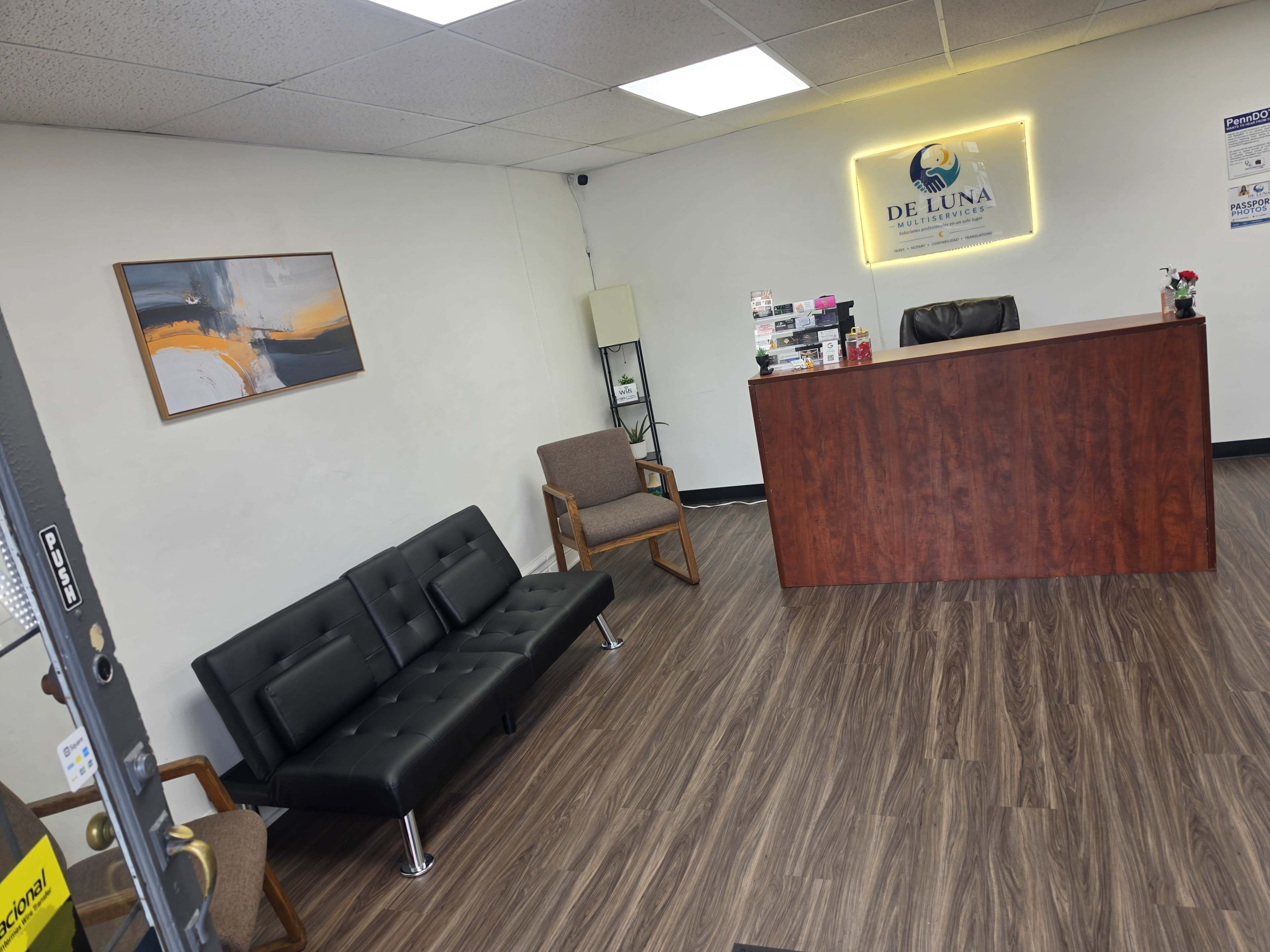 The image shows a reception area with a wooden front desk, two chairs, a painting on the wall, and neatly arranged promotional materials.
