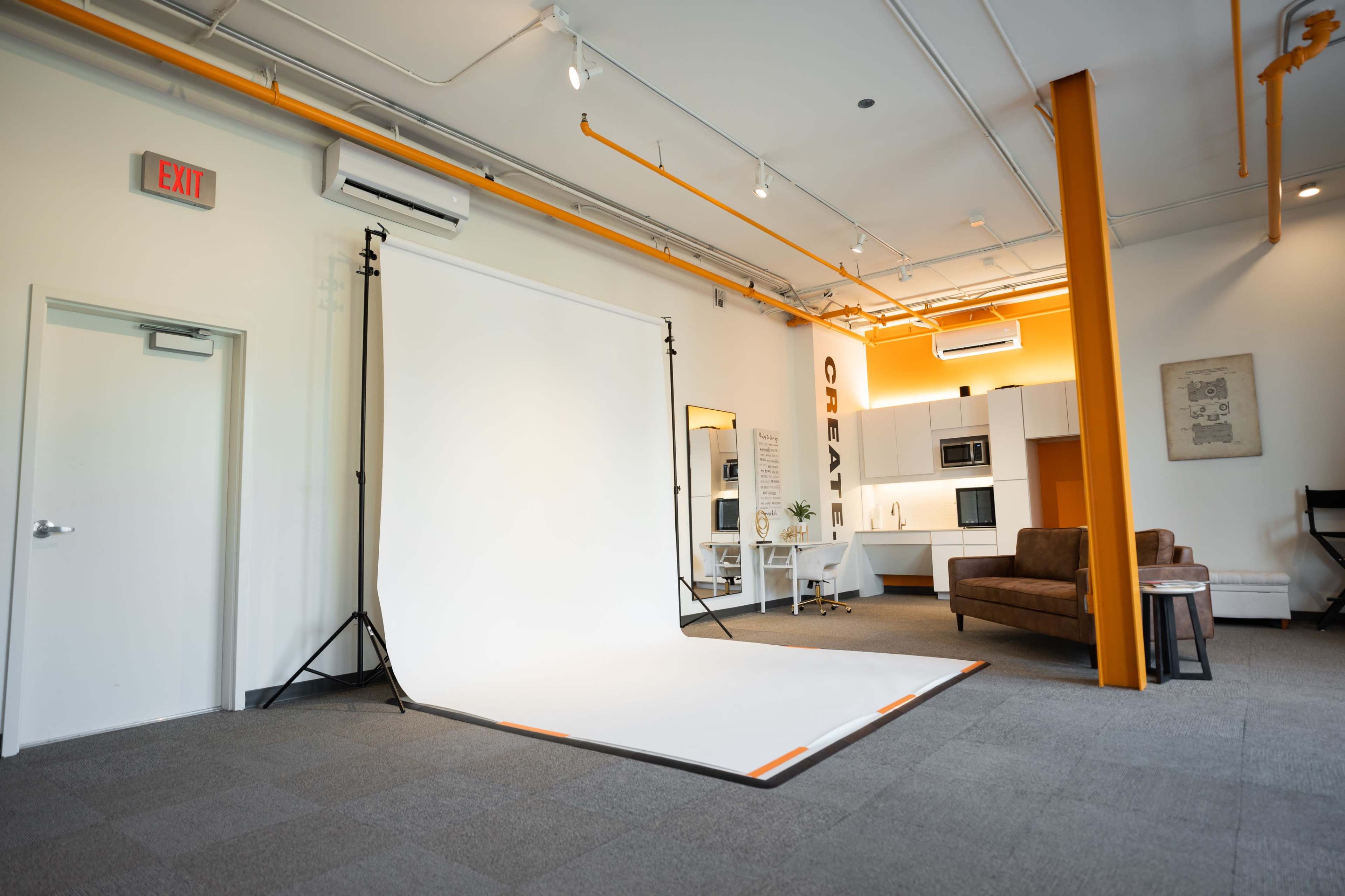 A spacious studio with a white backdrop, a brown couch, and a kitchenette in the background.
