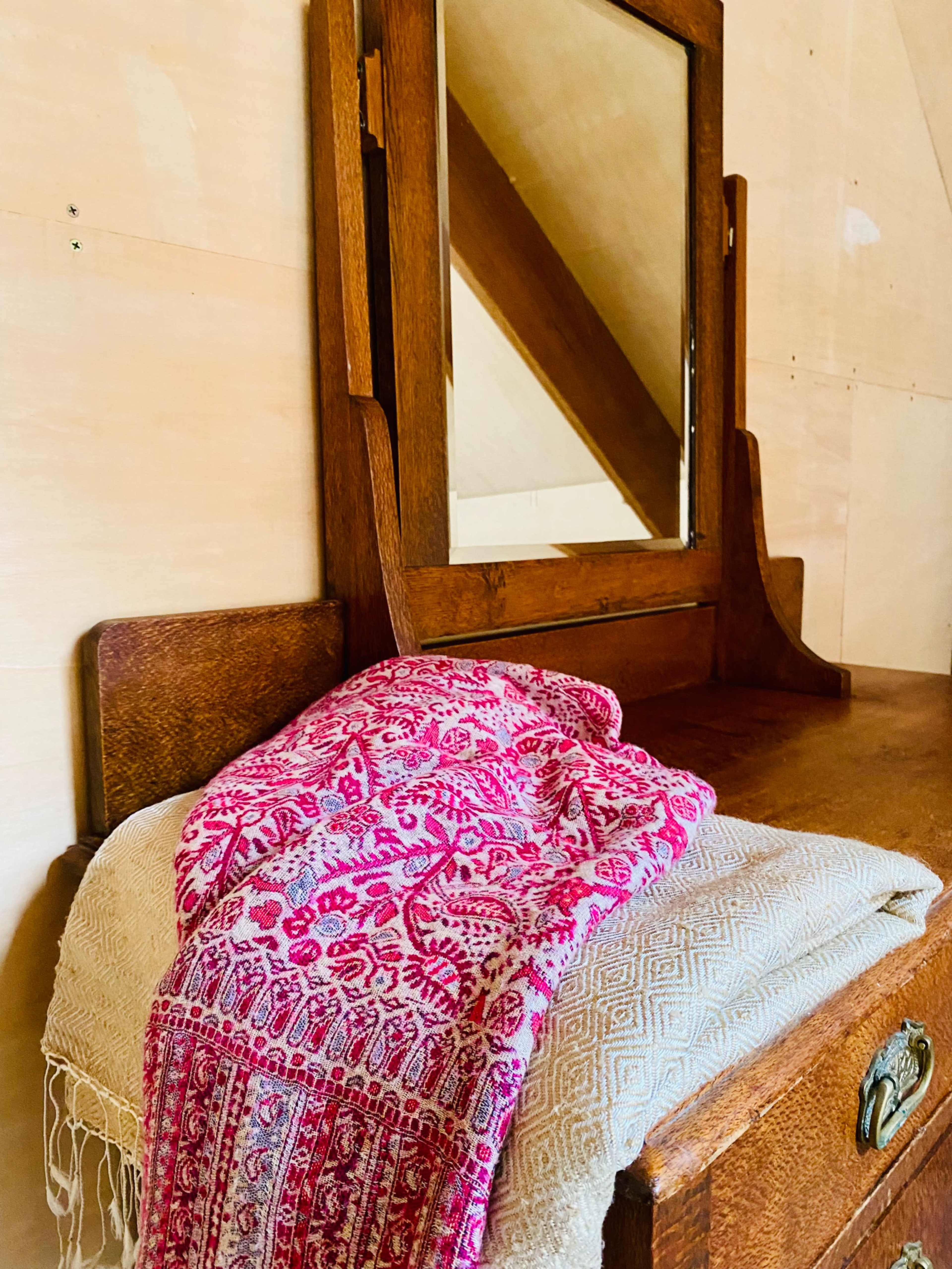 A wooden dresser with an upright mirror displays a folded patterned textile draped over its top.