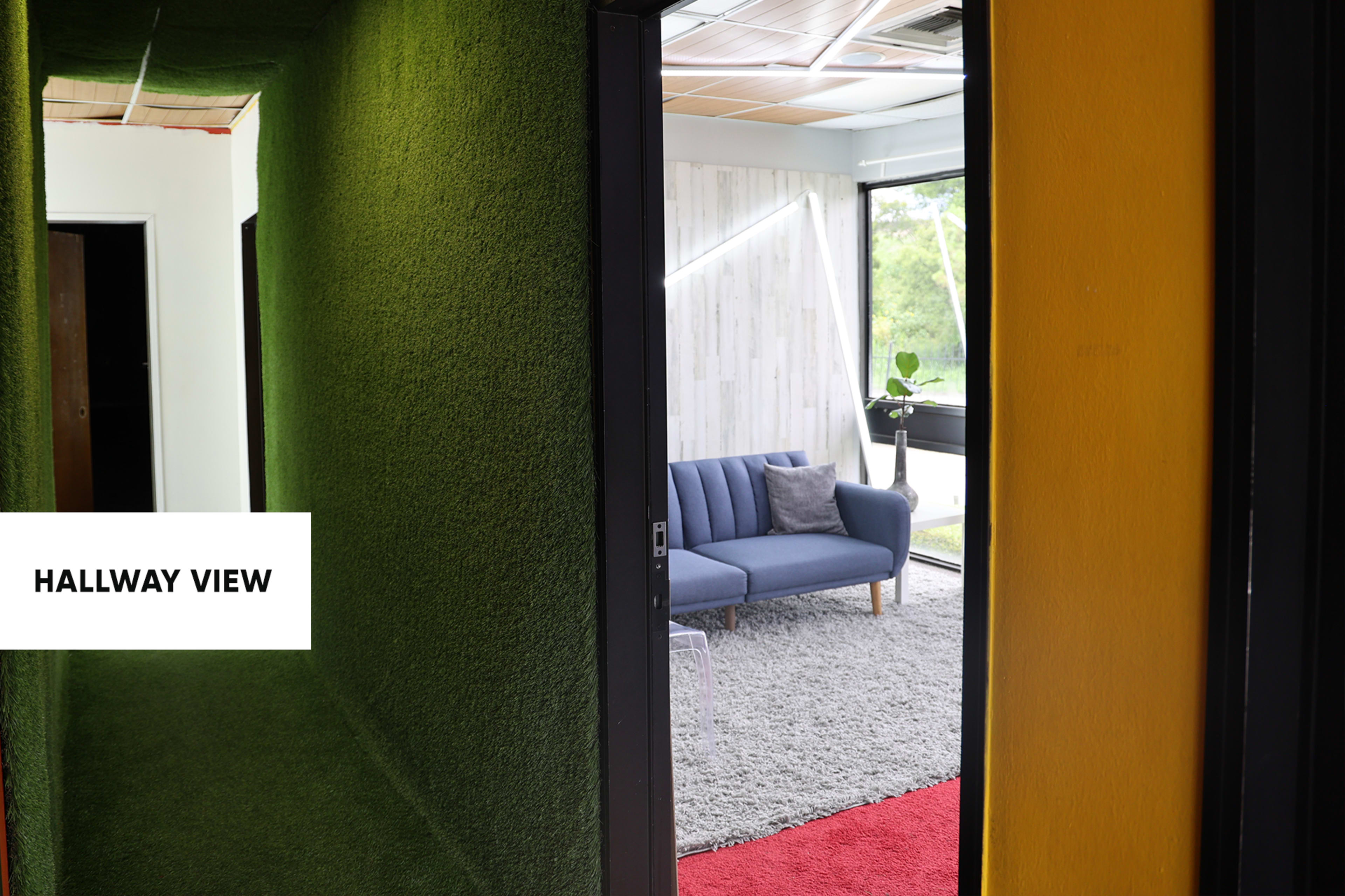 A hallway with green walls leading to a room that has a gray couch and large windows.