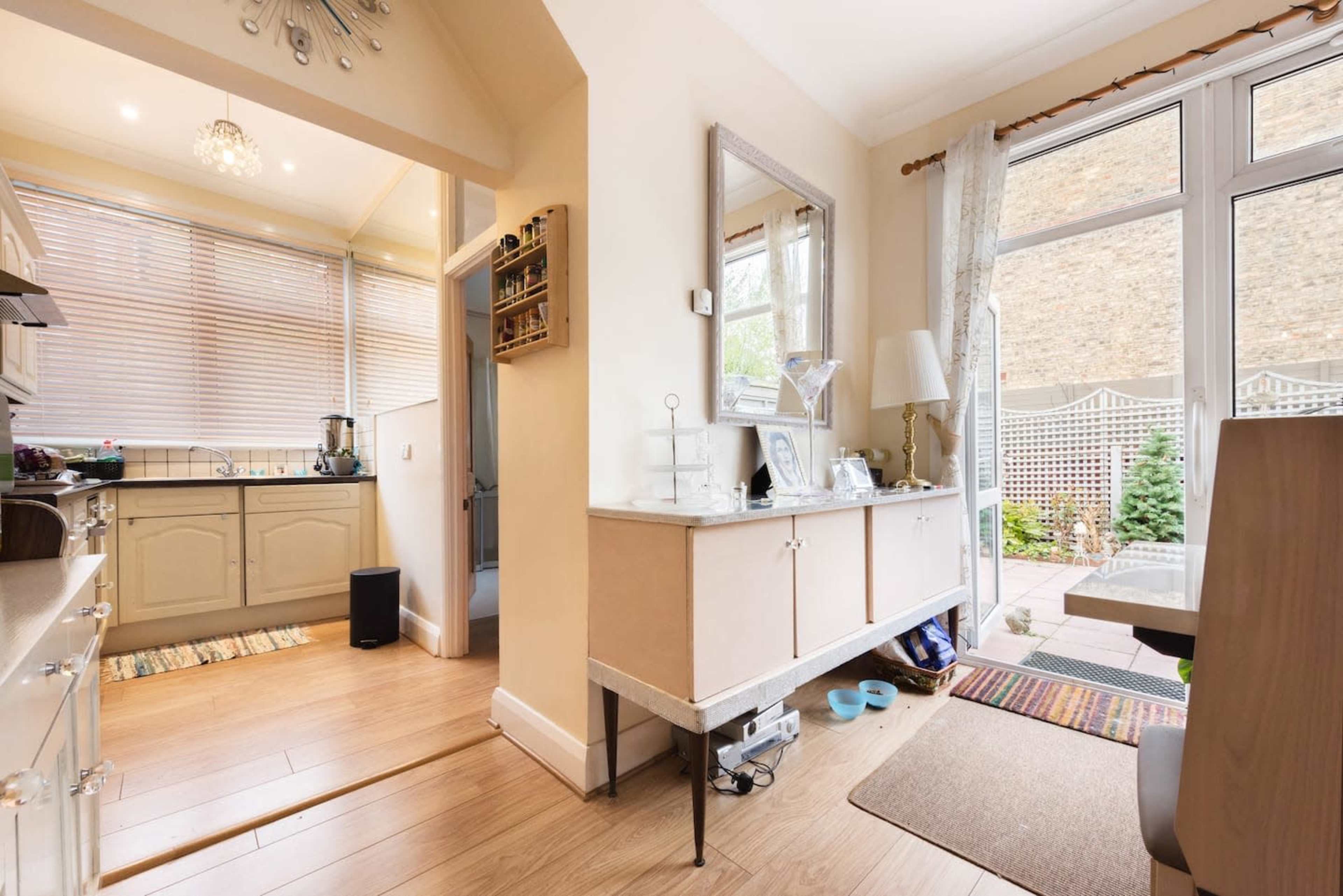 The image shows a modern kitchen area with light-colored cabinetry, a mirror on the wall, and large windows leading to a small outdoor space.