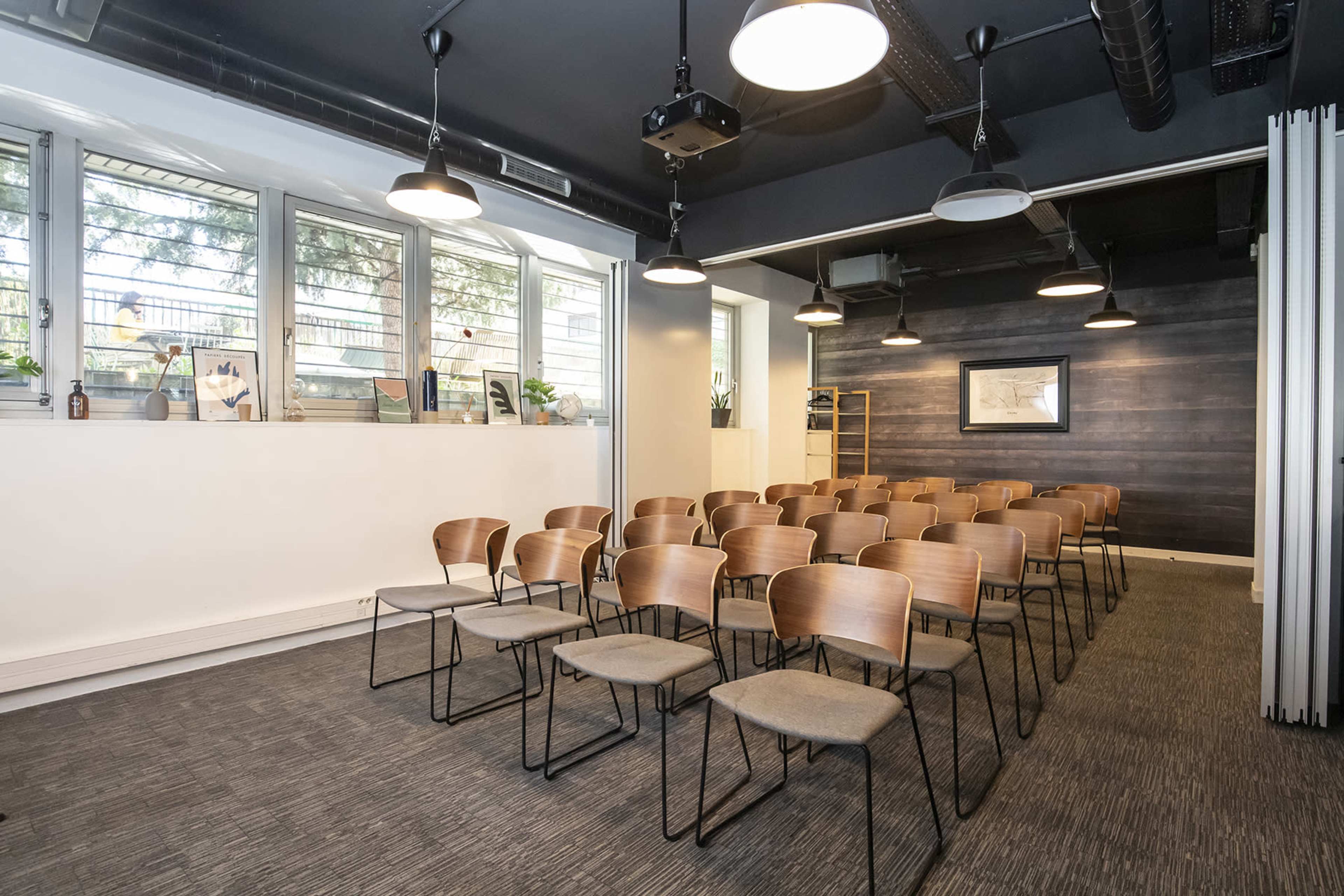 A modern meeting room with several rows of wooden chairs arranged facing a wall with framed artwork.