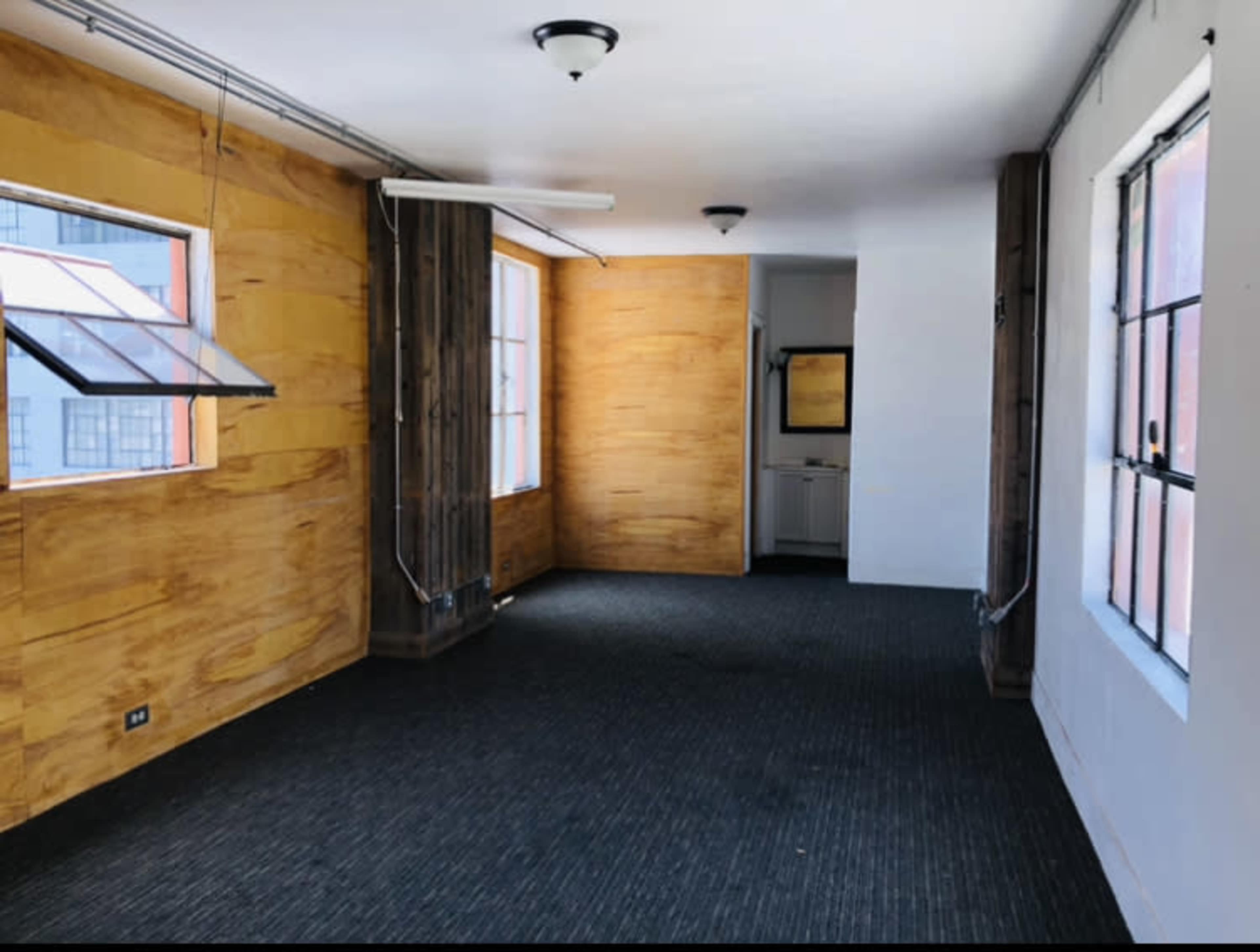 An empty room with wooden walls, carpeted flooring, and large windows.