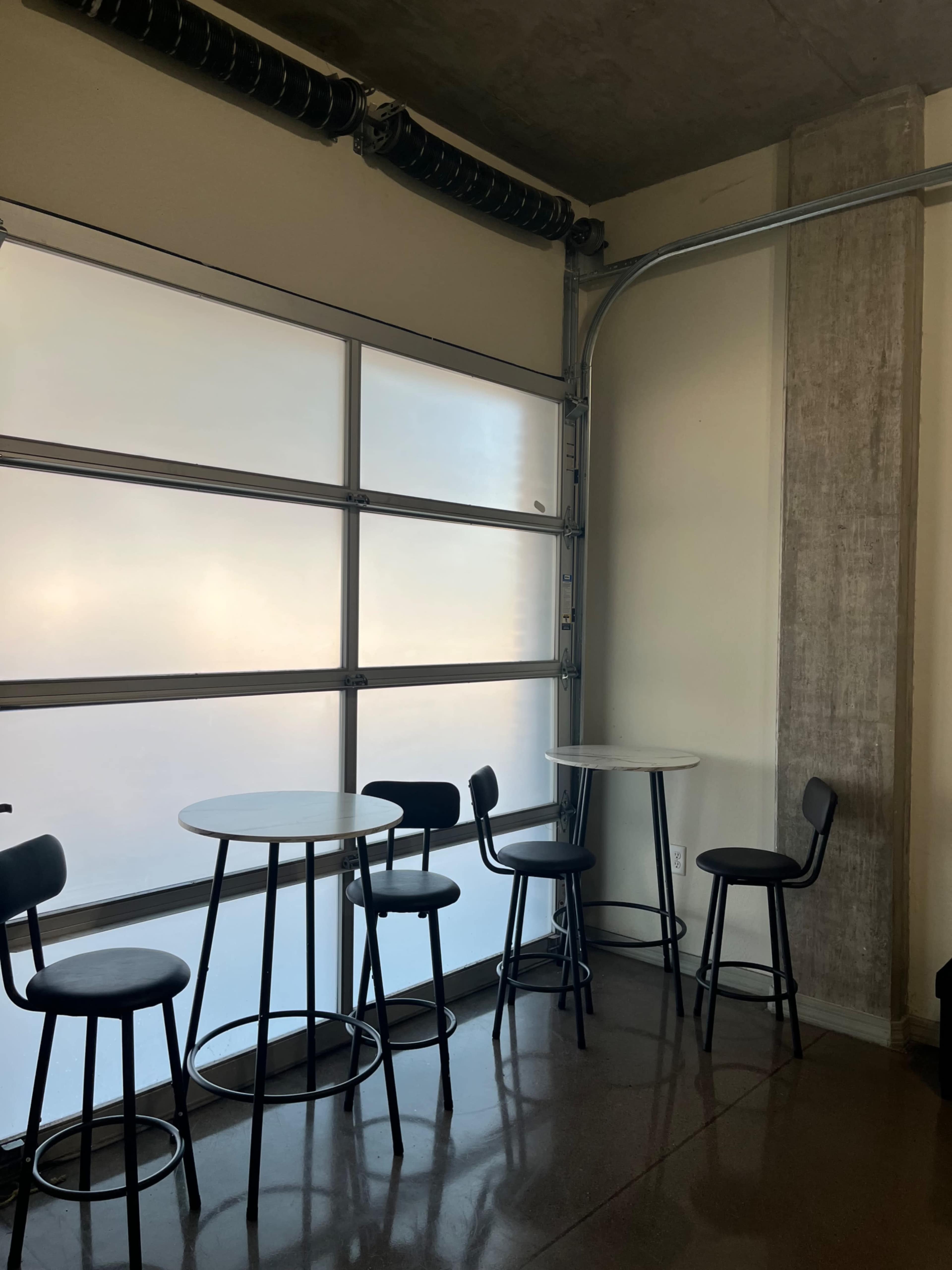 A small seating area features two round tables and chairs next to a large garage-style window.
