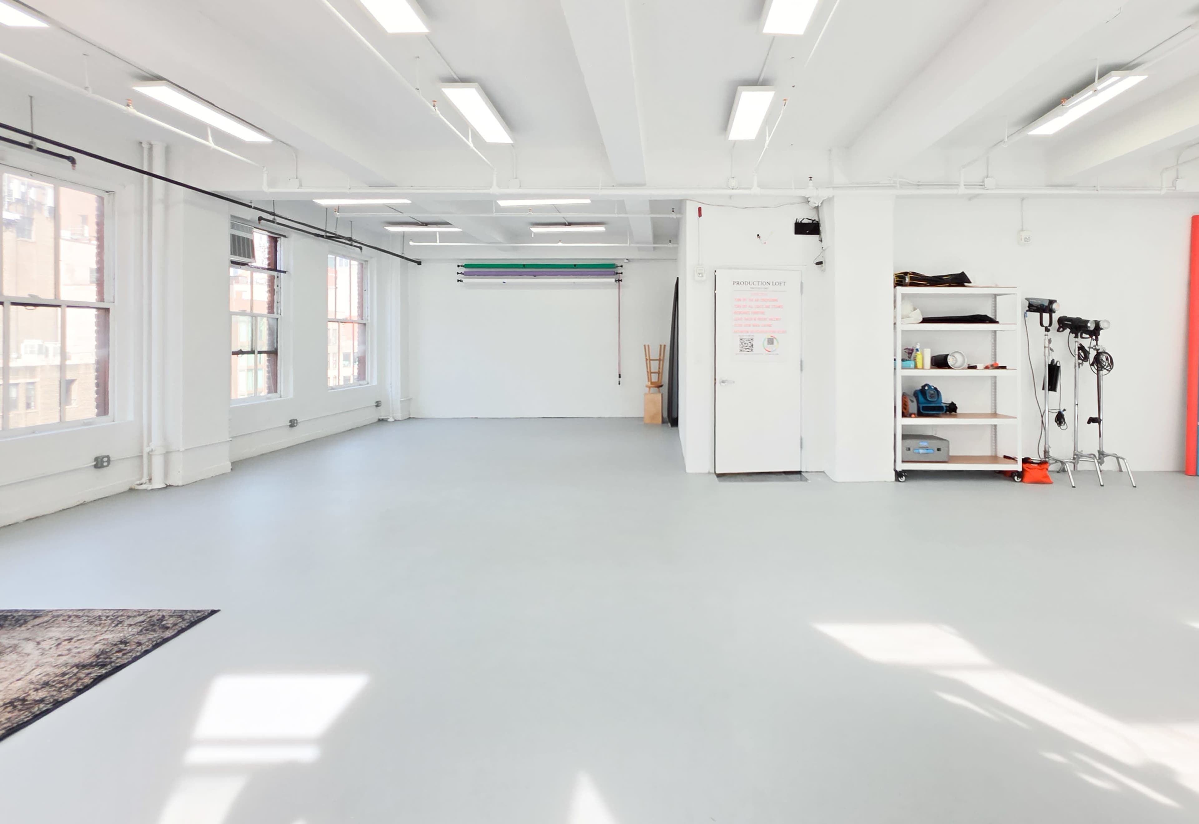 The image shows a spacious, empty room with white walls, a light gray floor, and natural light coming through large windows.
