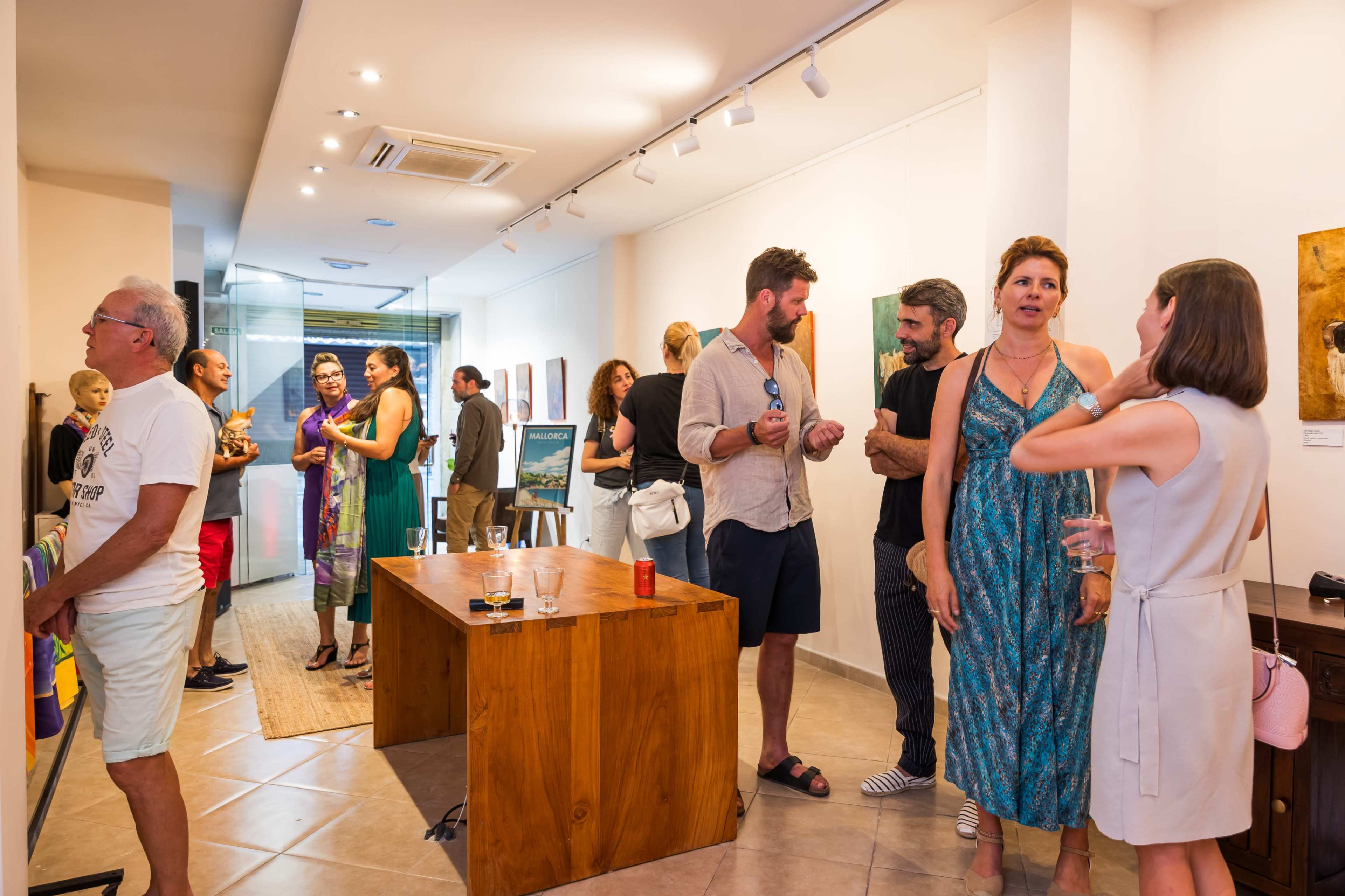 A group of people socialize in an art gallery, discussing artworks and enjoying refreshments.