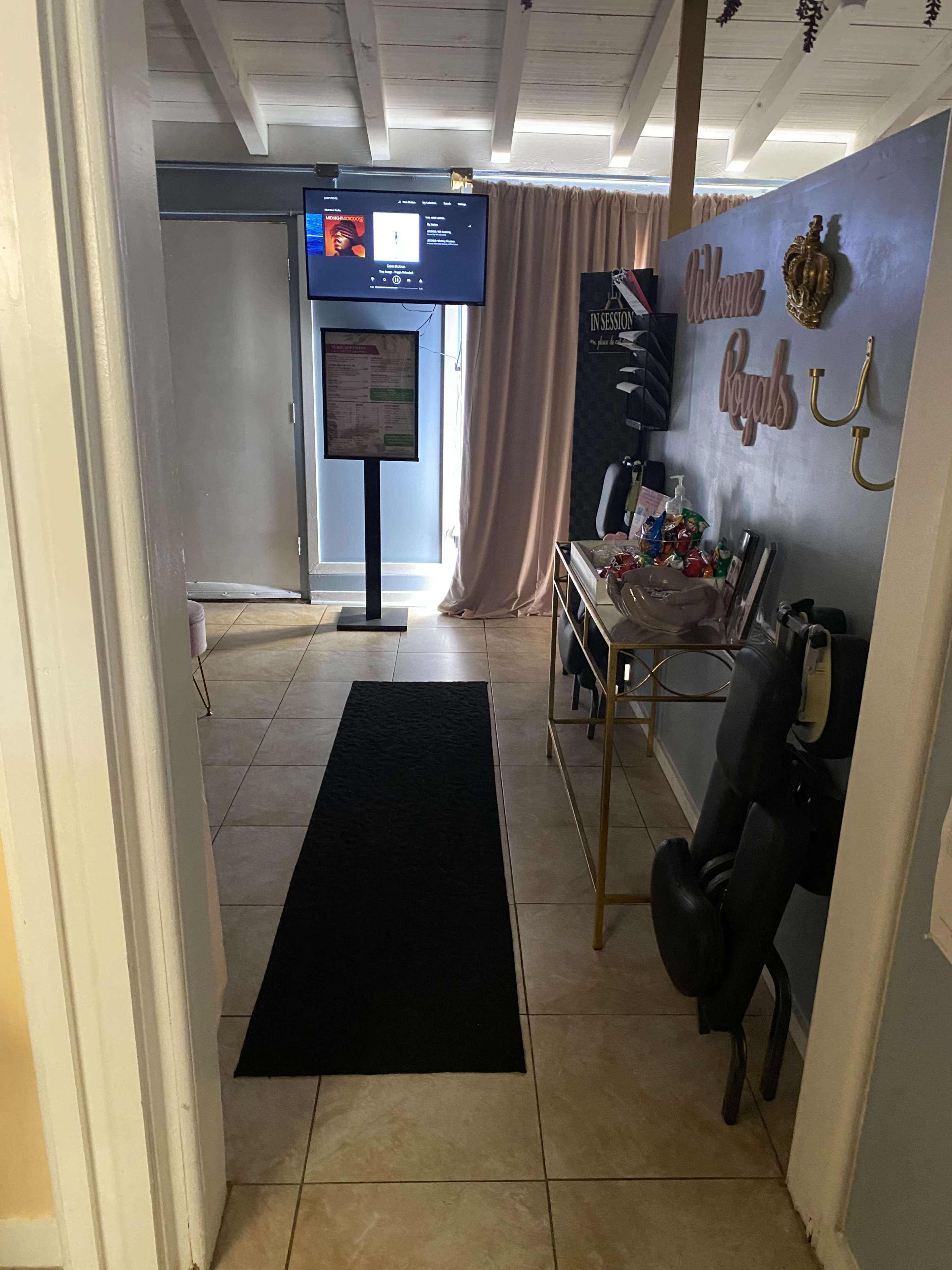 A hallway leading to a room with a large screen on a stand, a black carpet runner, and a welcoming decor on the walls.