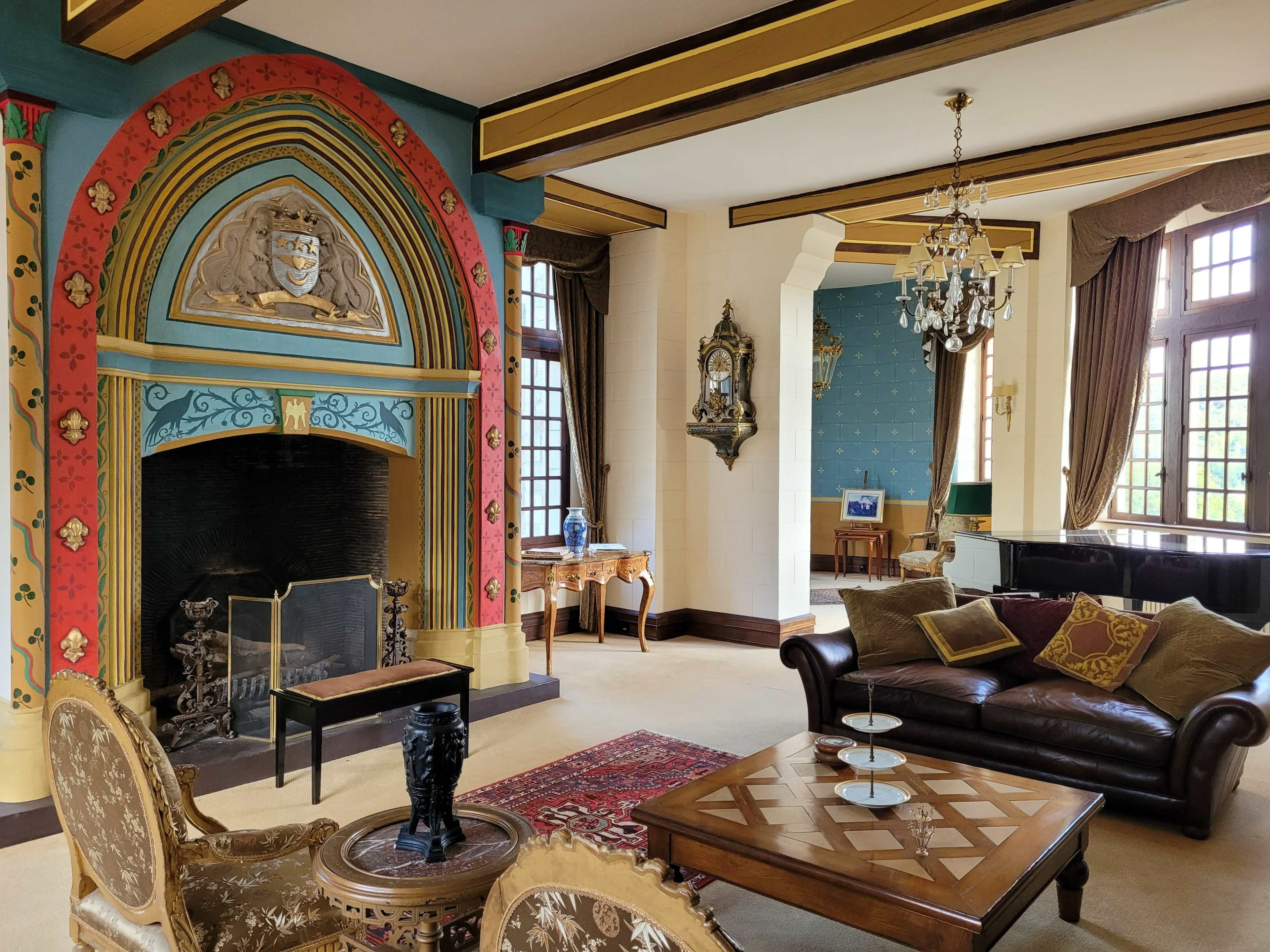 An ornate living room with a colorful fireplace, elegantly decorated furniture, and large windows allowing natural light to enter.